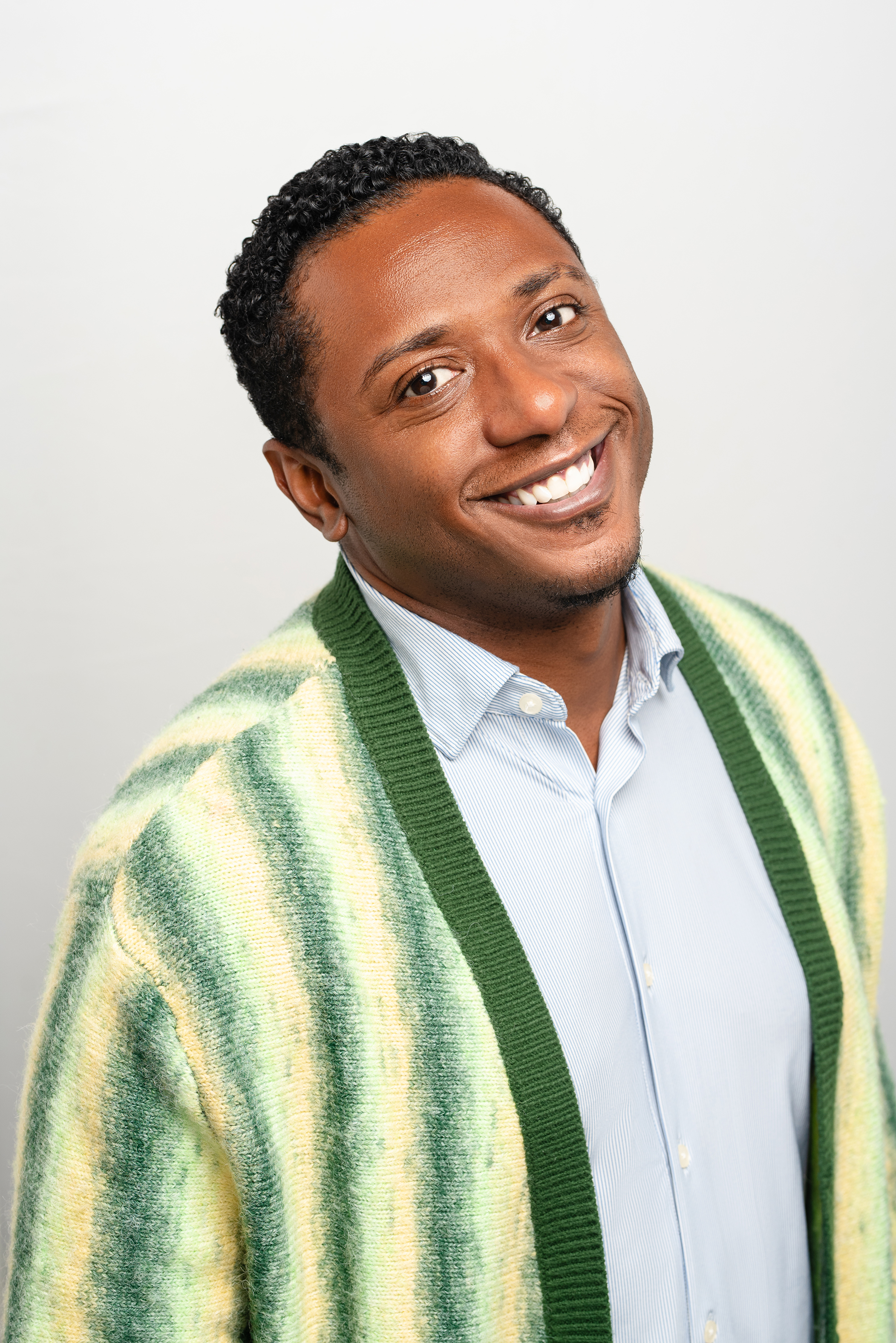 Professional portrait of a smiling man in a striped jacket against a light background