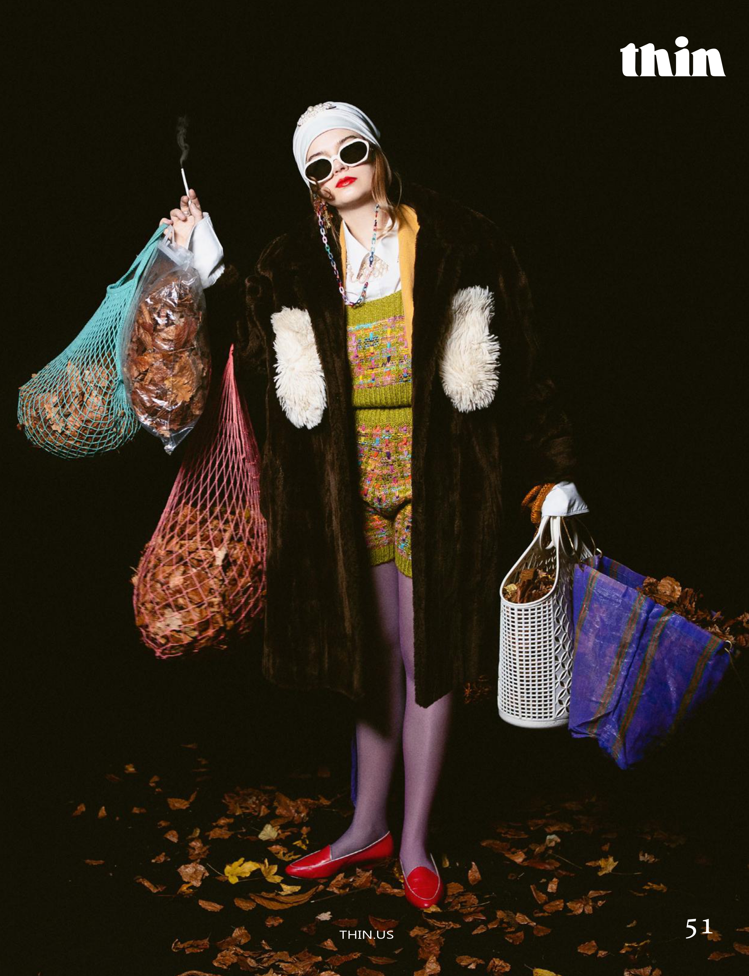Fashion editorial image of a model in eclectic layered styling holding several bags against a dark background.
