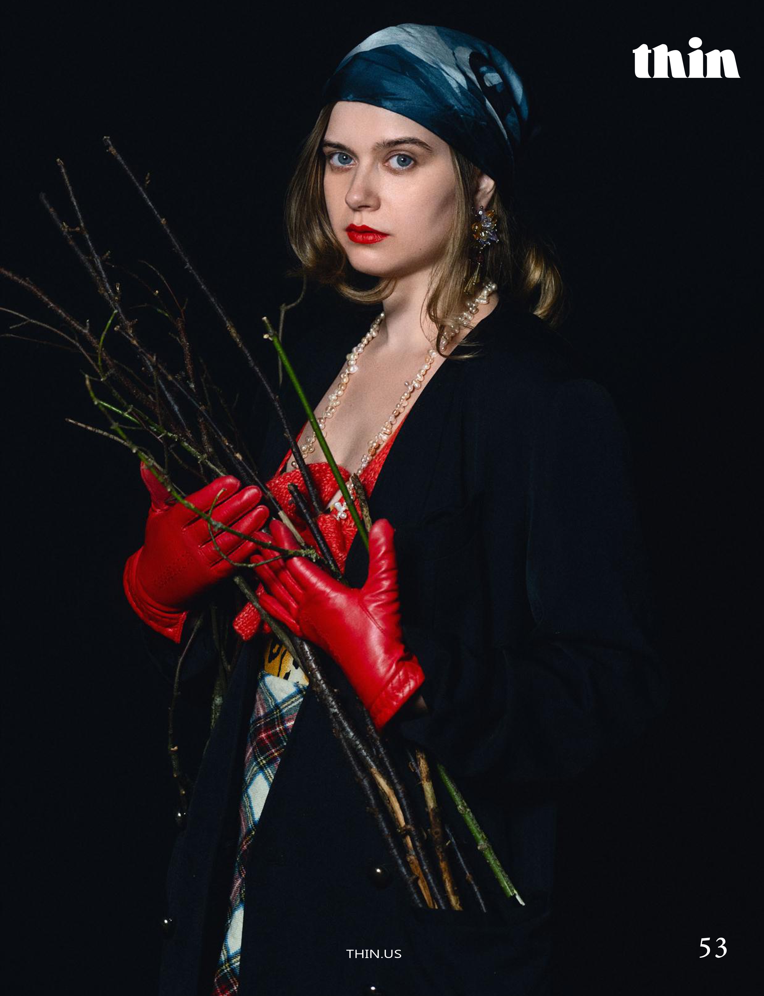 Editorial portrait of a woman in red gloves and a dark headscarf holding bare branches.