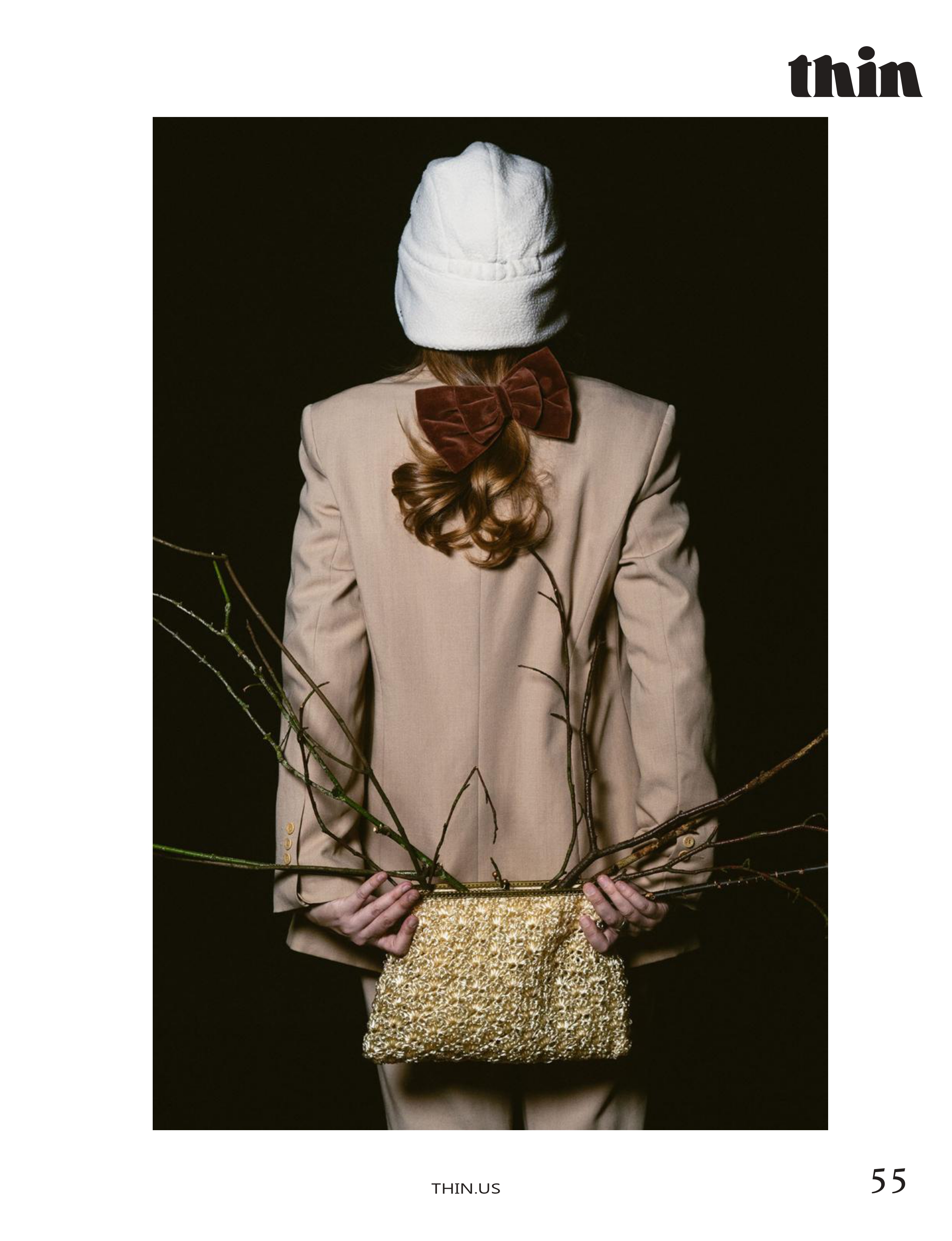 Back view of a model in an oversized beige suit holding branches and a textured handbag.