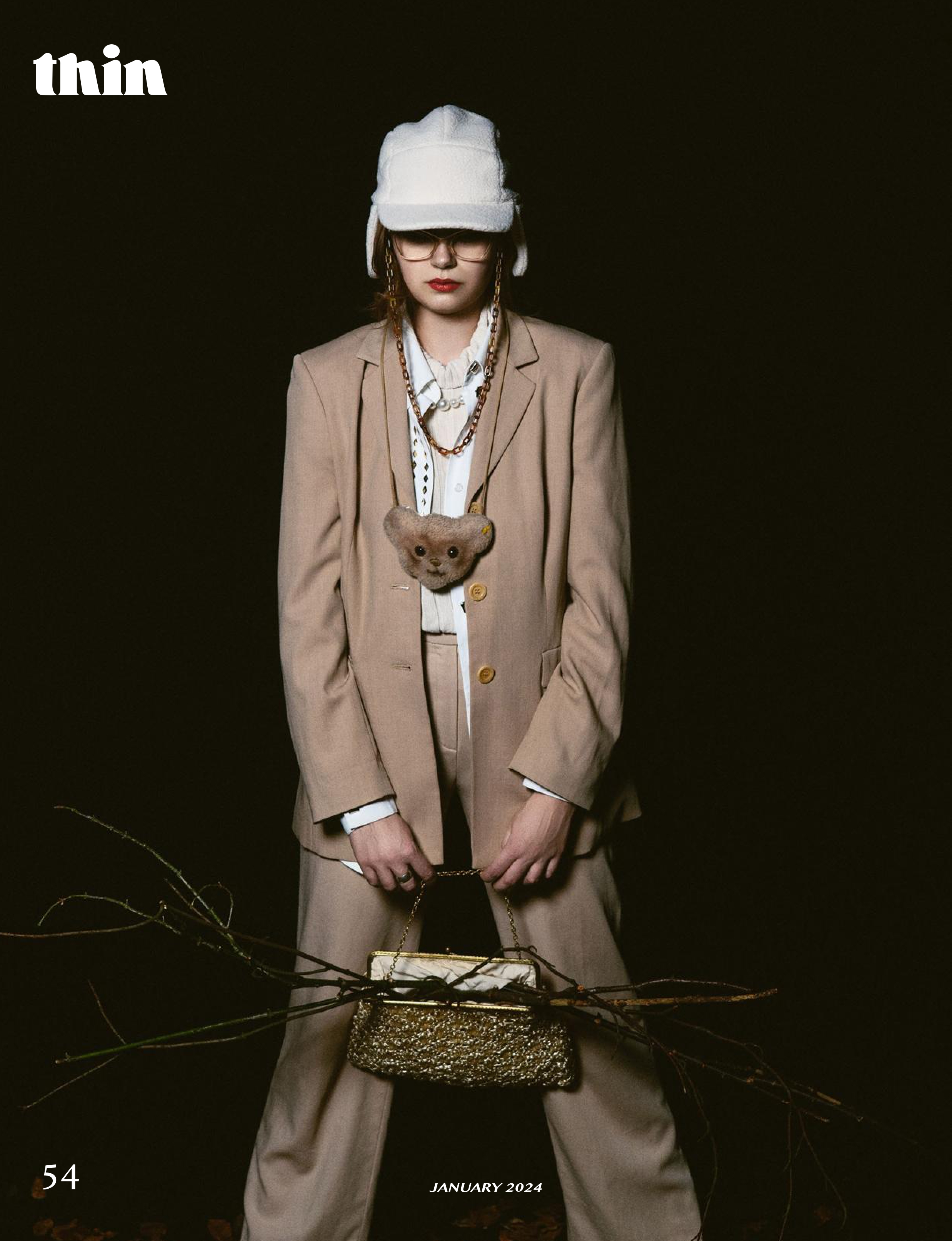 Fashion portrait of a model in an oversized beige suit, white head covering and layered accessories.