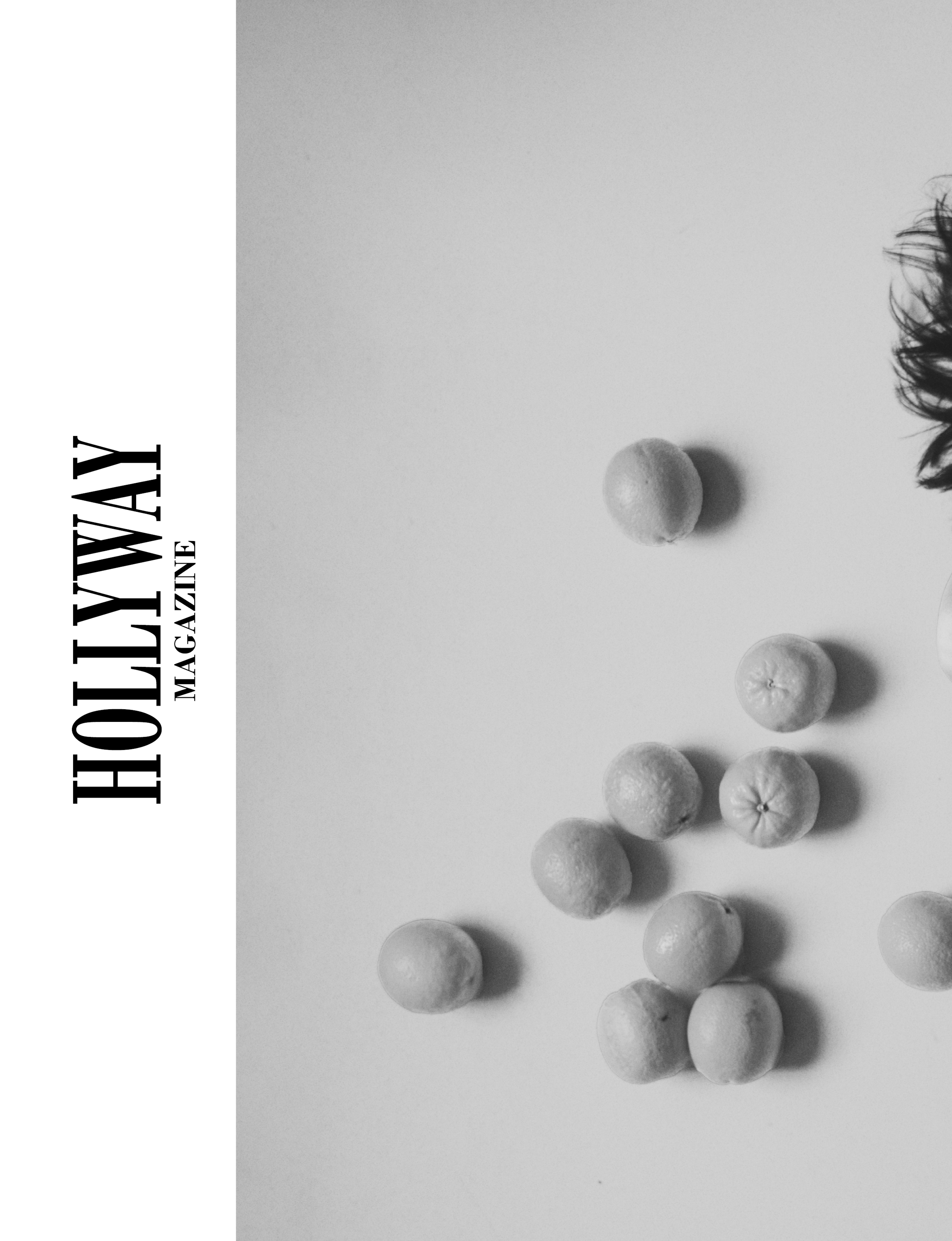 Minimal black-and-white editorial image of scattered oranges and part of a figure entering the frame.