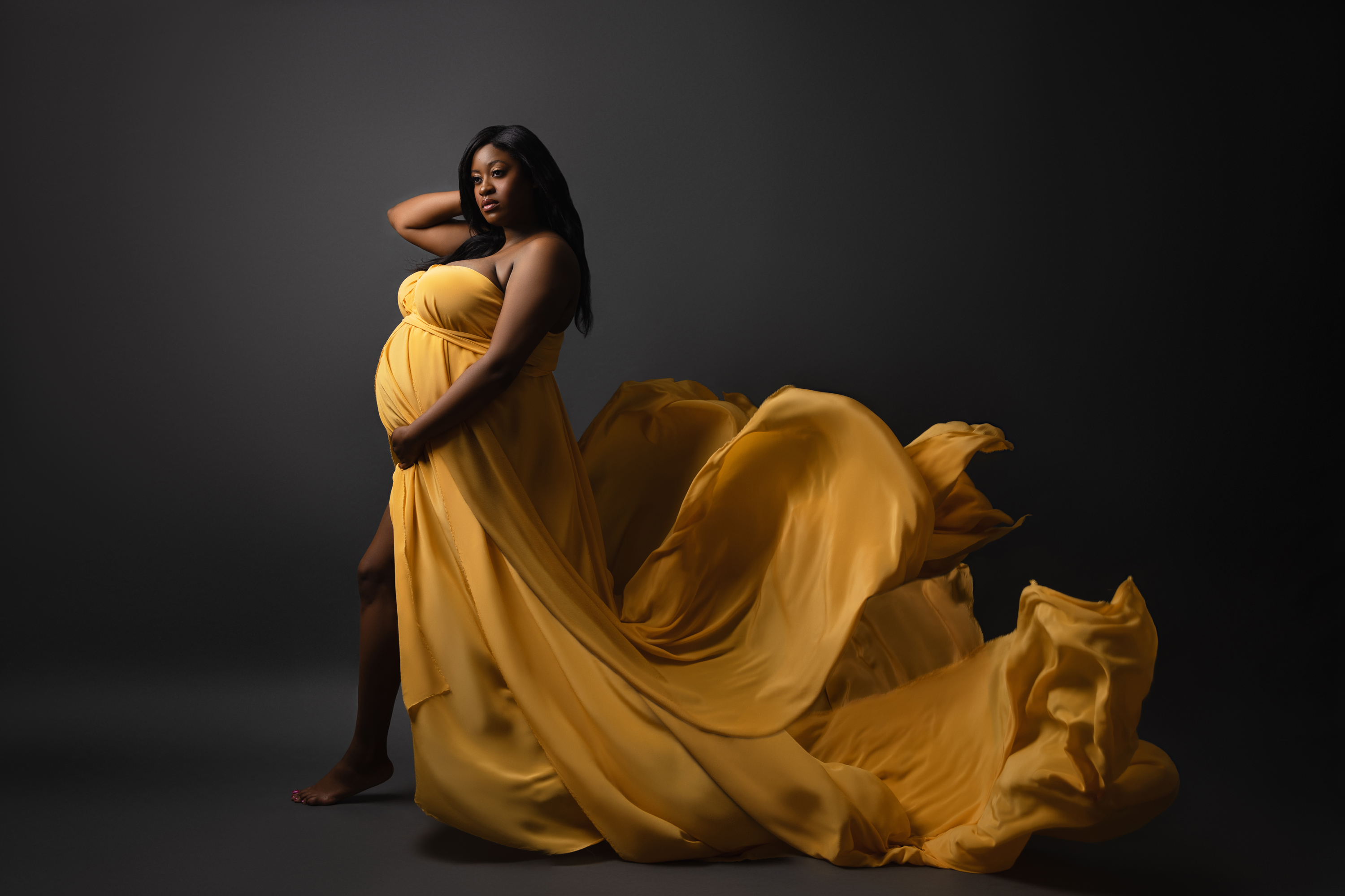 Reclining maternity portrait in a rich gold gown photographed with low-key studio lighting.