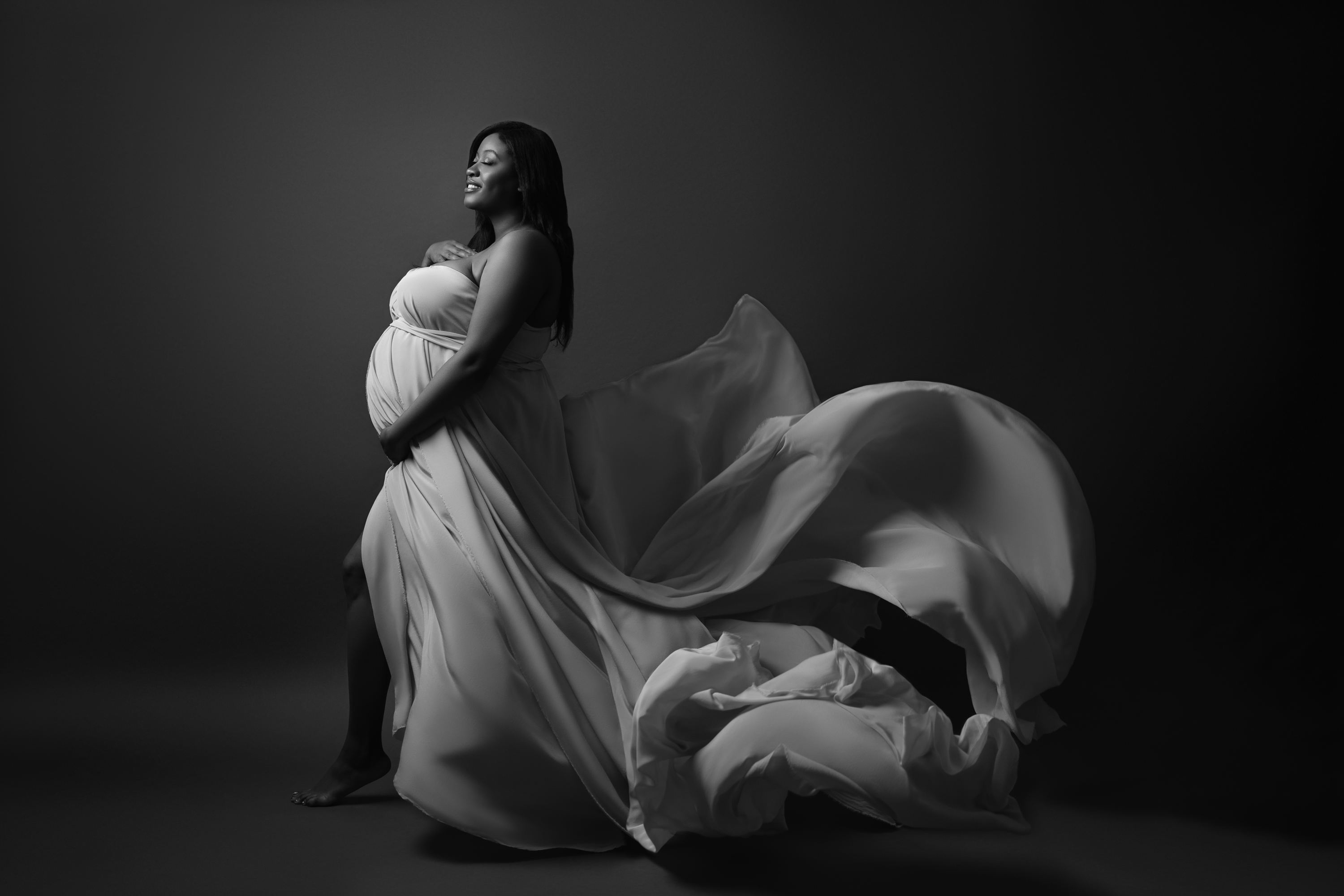Black-and-white maternity portrait with sculptural posing and dramatic directional light.