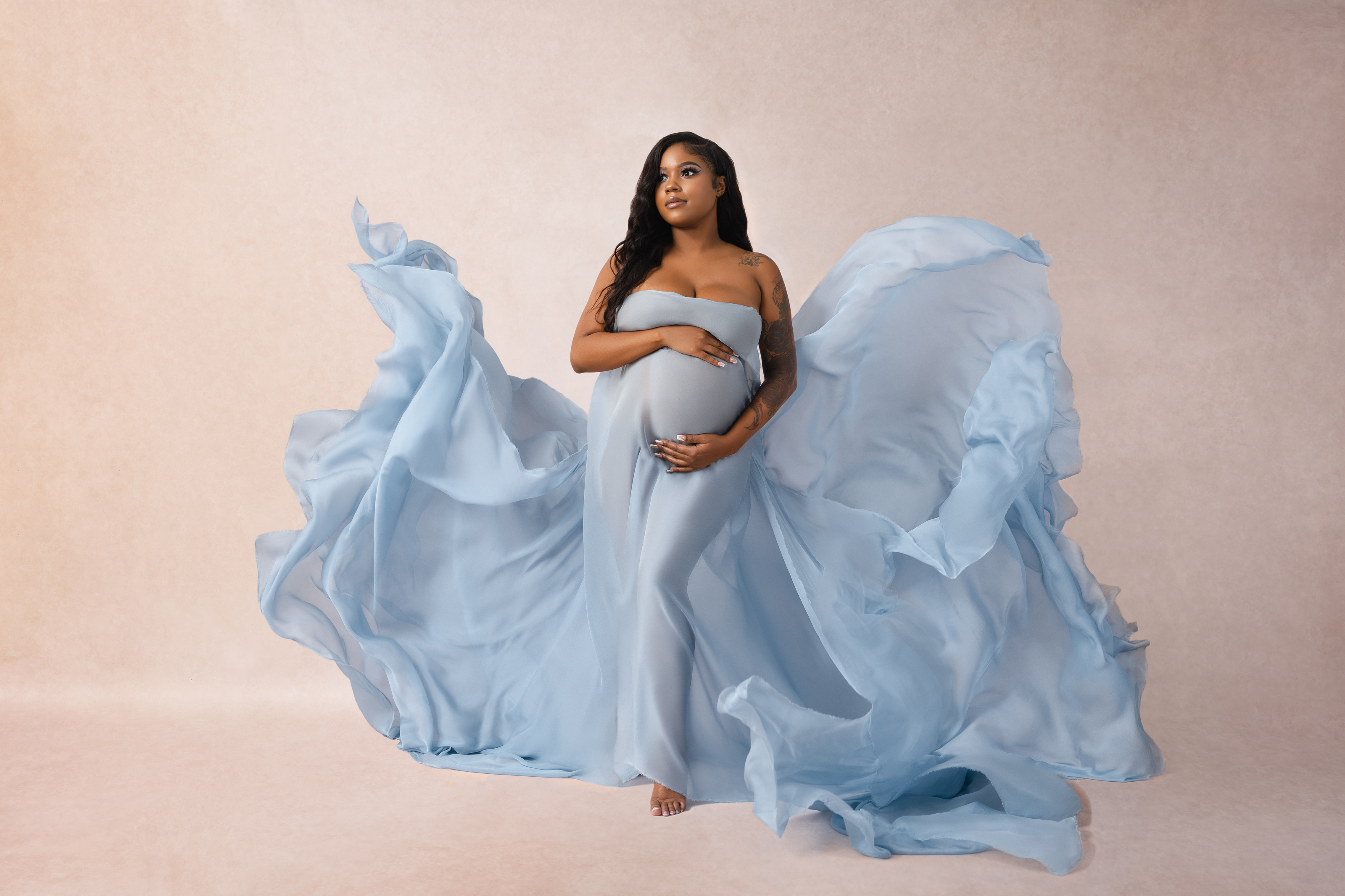 Full-length maternity portrait with a pale blue gown captured in motion against a soft blush background.