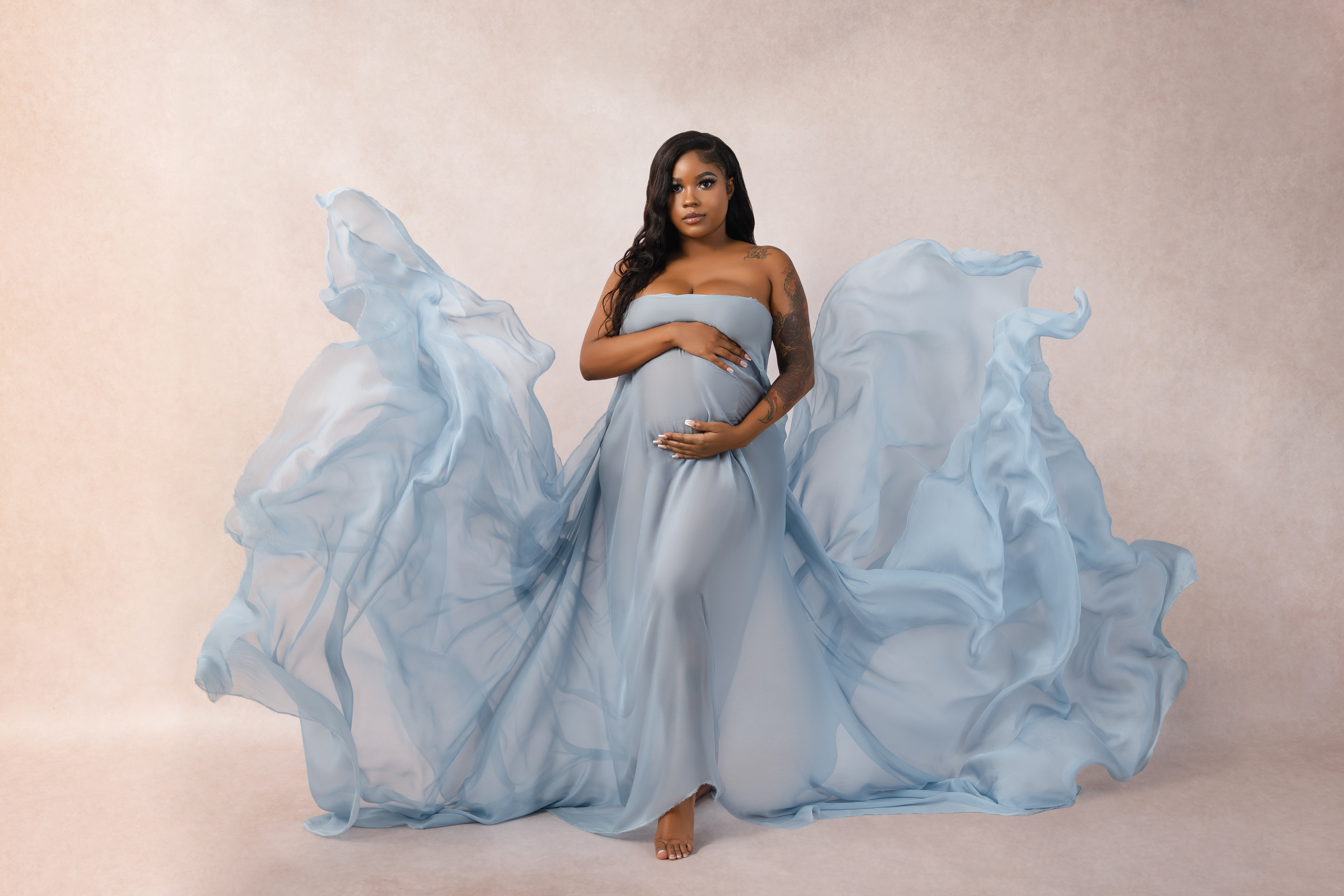 Studio maternity portrait with a pale blue gown spreading outward in dramatic flowing shapes.