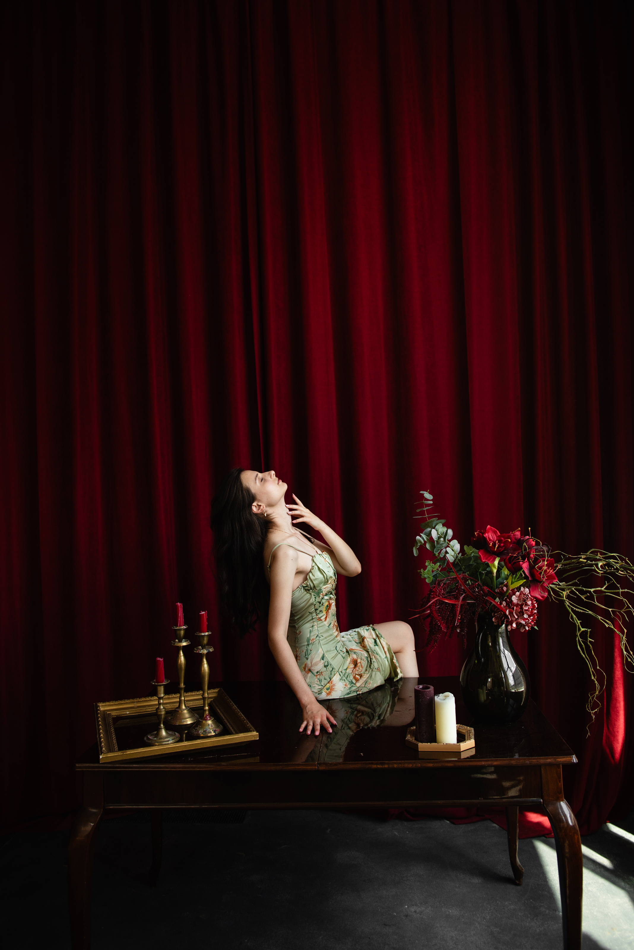 Unretouched portrait of a woman posing on a table against red curtains in a dark studio set.
