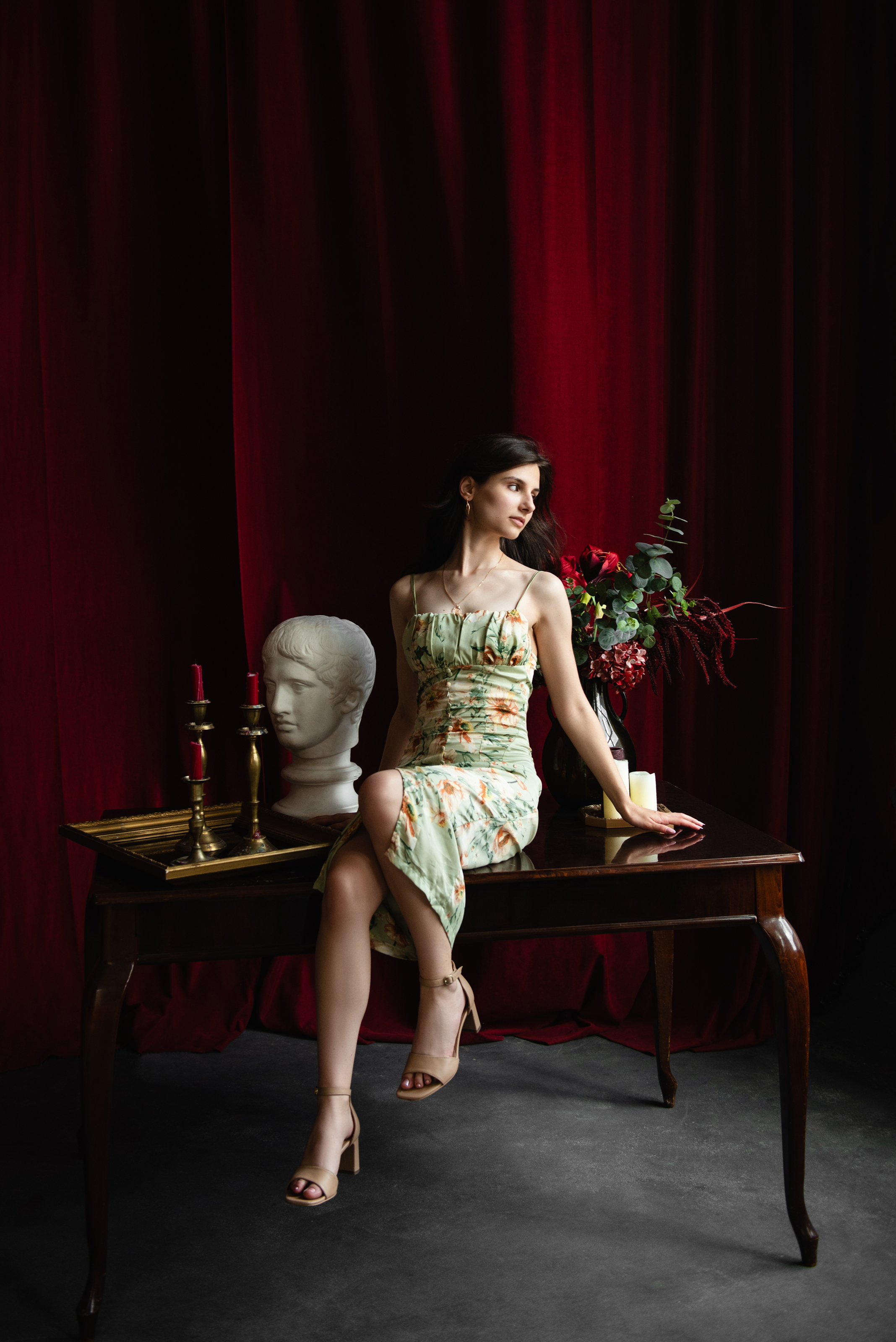 Unretouched full-length portrait of a woman seated on a wooden table against red studio curtains.