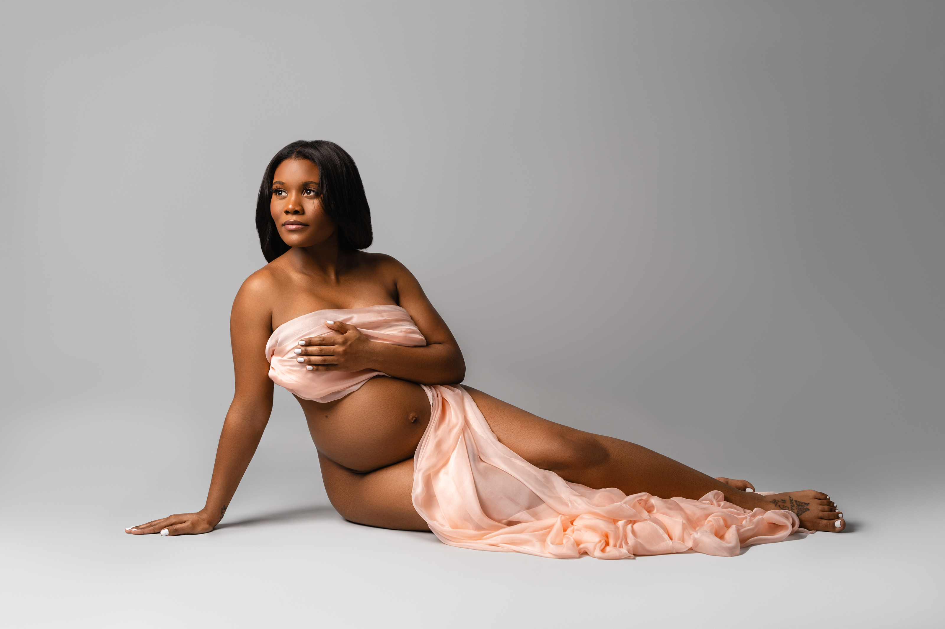 Side maternity portrait with flowing peach fabric and soft neutral studio lighting.