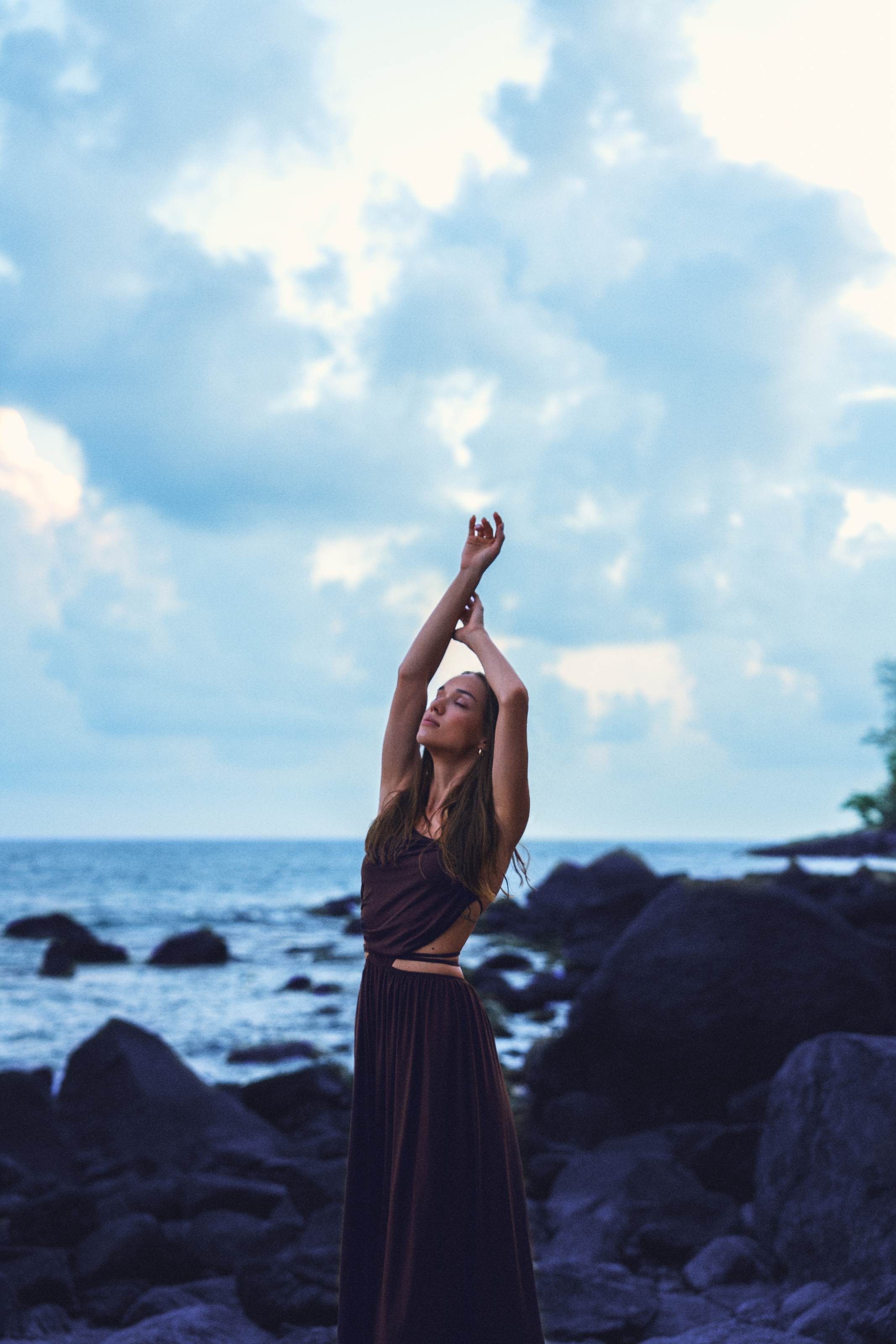 Moody coastal portrait of a woman in a dark flowing dress with cool blue tones and twilight-inspired color grading