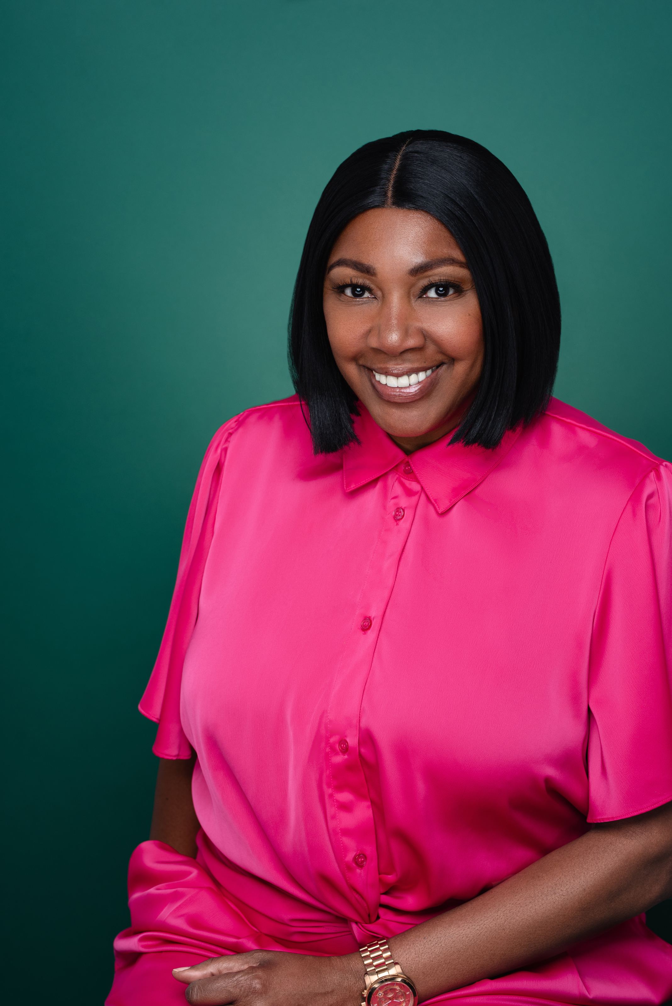 Studio portrait of a smiling woman in a bright pink outfit against a deep green background