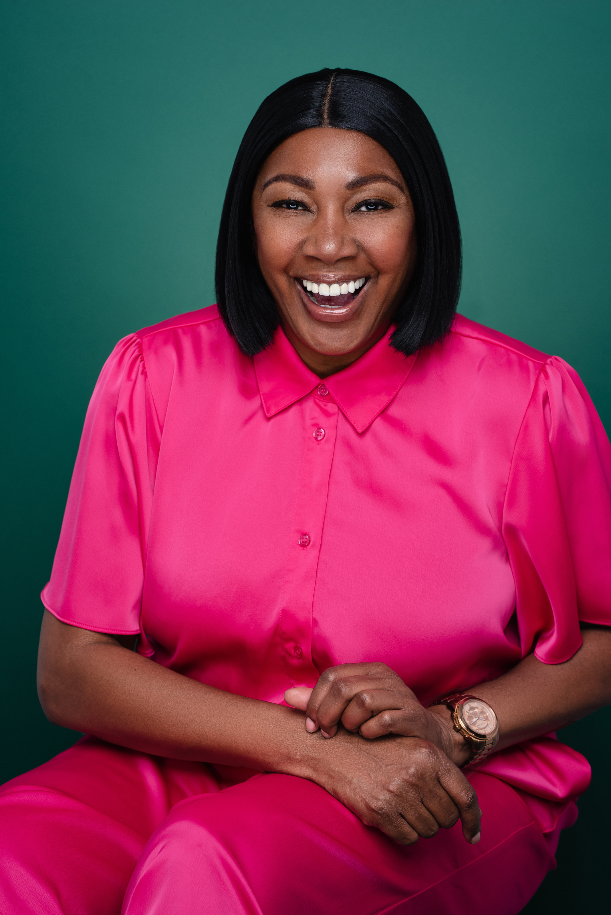 Joyful studio portrait of a woman laughing in a bright pink outfit against a deep green background