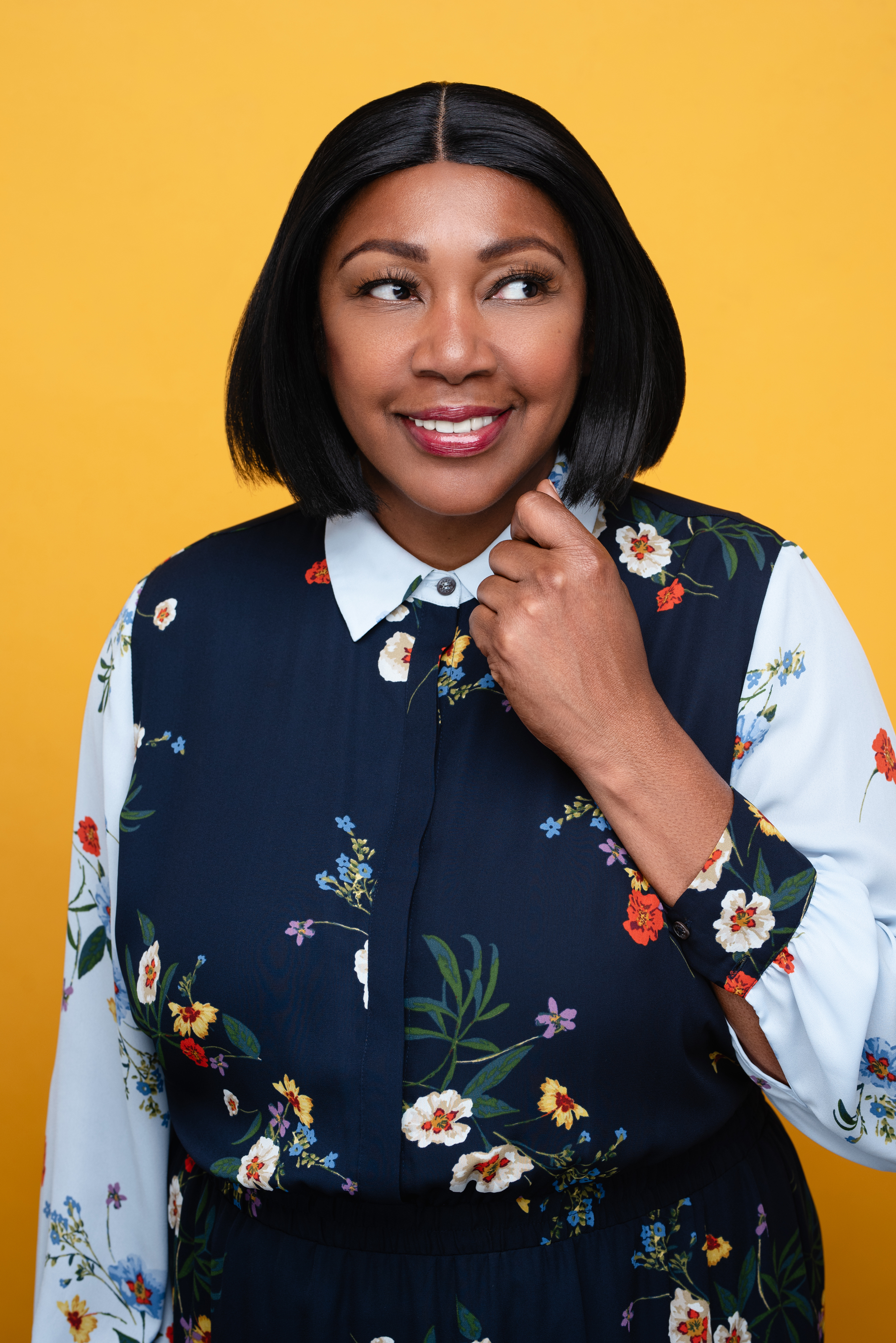 Studio portrait of a smiling woman in a floral blouse against a warm yellow background
