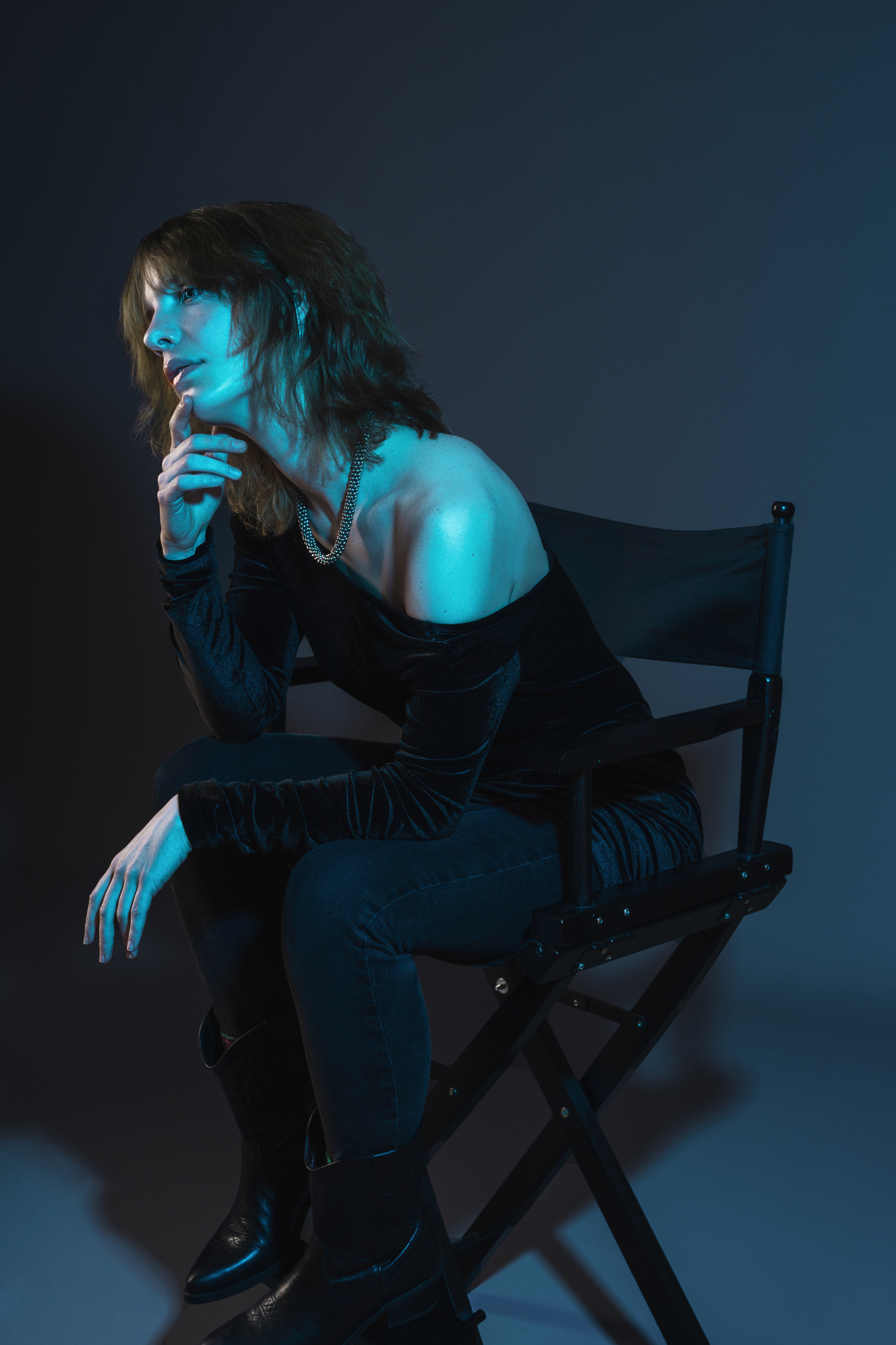 Moody studio portrait of a woman seated in a director chair under cool cyan lighting