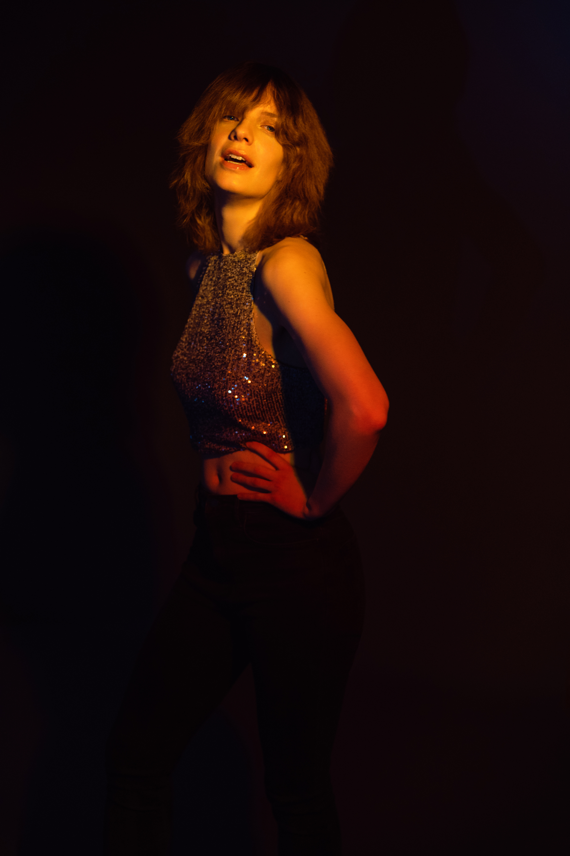 Expressive studio portrait of a smiling woman in a shimmering top under dramatic warm lighting