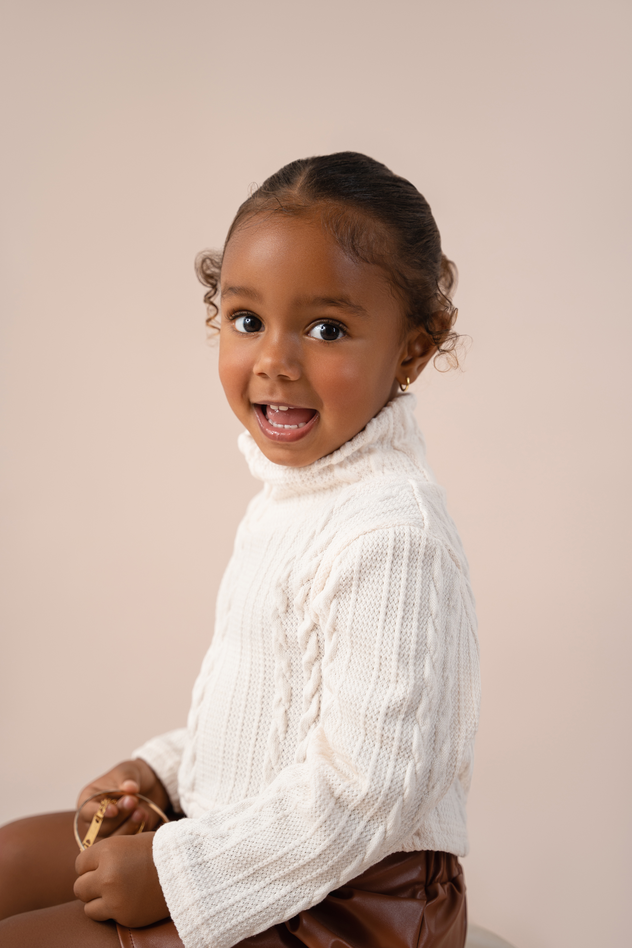 Studio portrait of a smiling young girl in a white sweater and brown skirt against a soft beige background