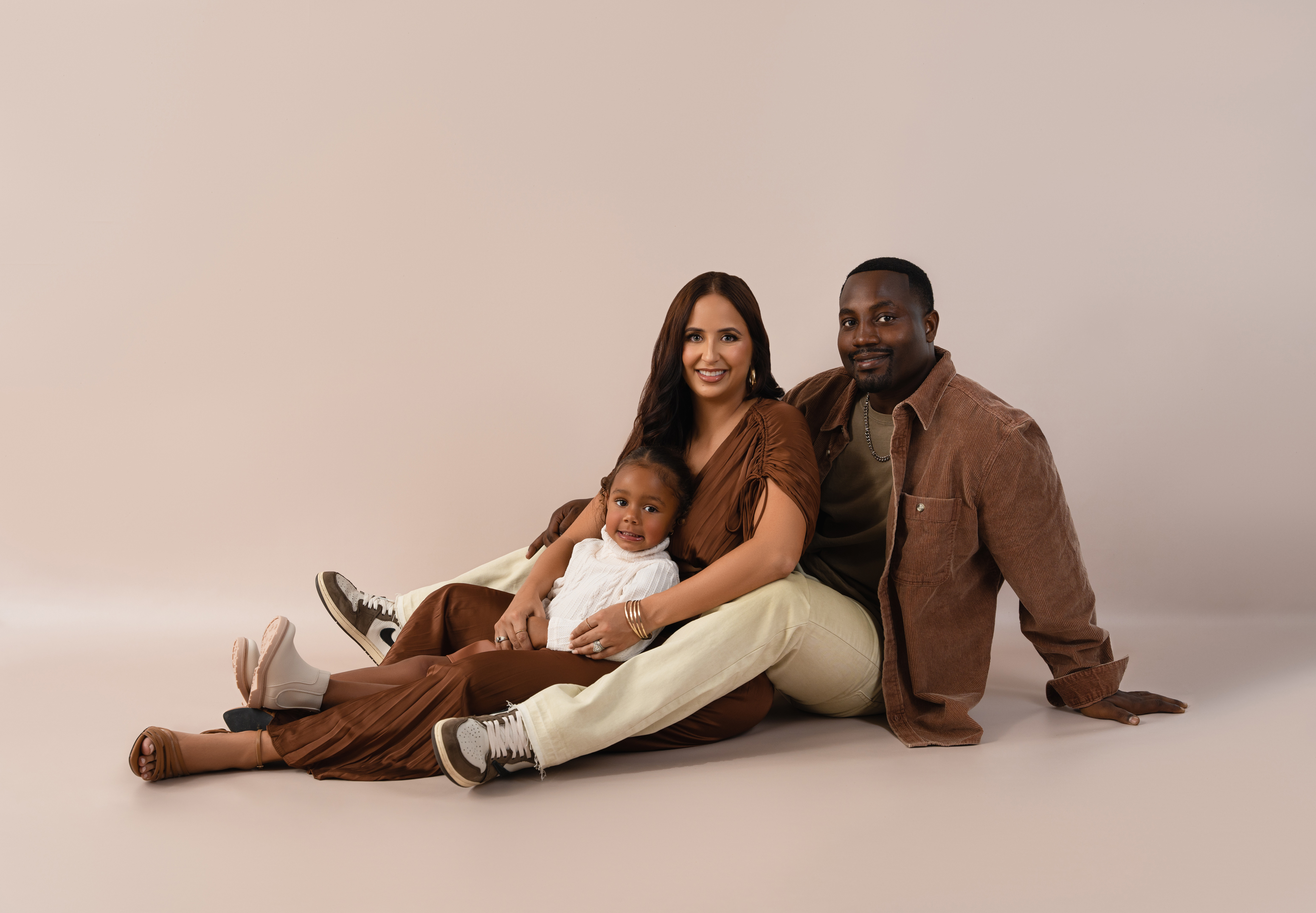 Relaxed family portrait of two parents and their young daughter seated together on a studio floor