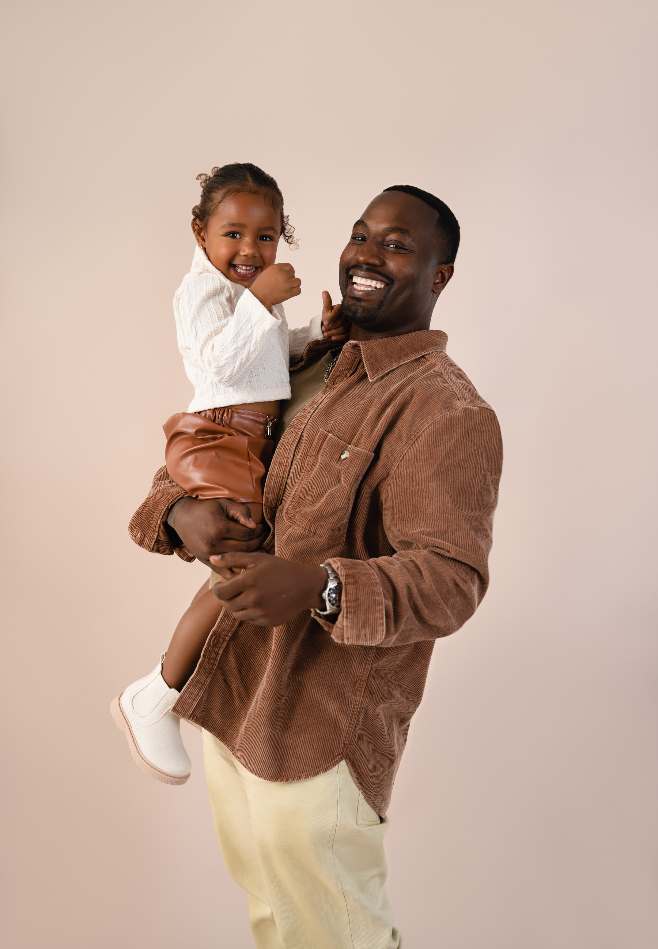 Warm studio portrait of a smiling father holding his young daughter against a neutral beige background