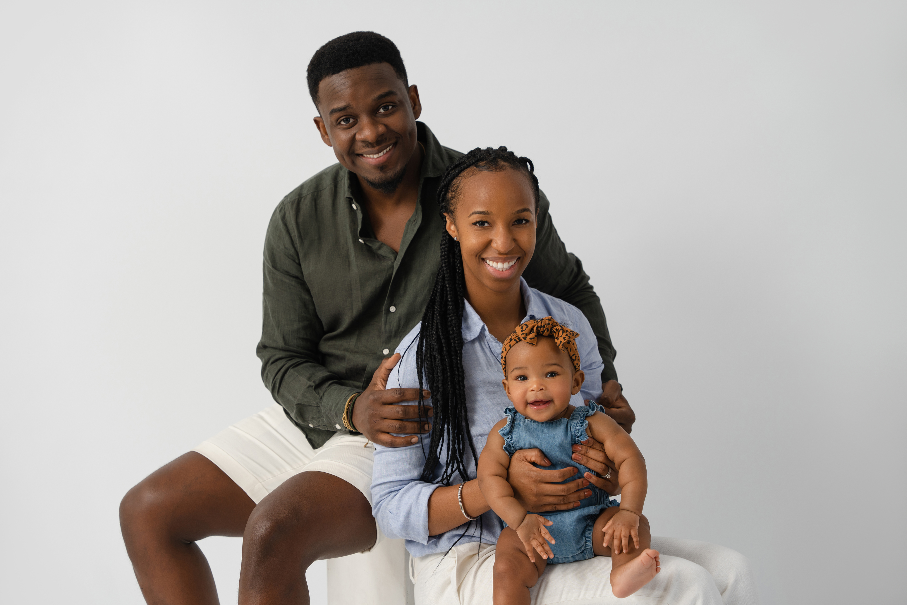 Studio family portrait of two parents with their baby against a clean light gray background
