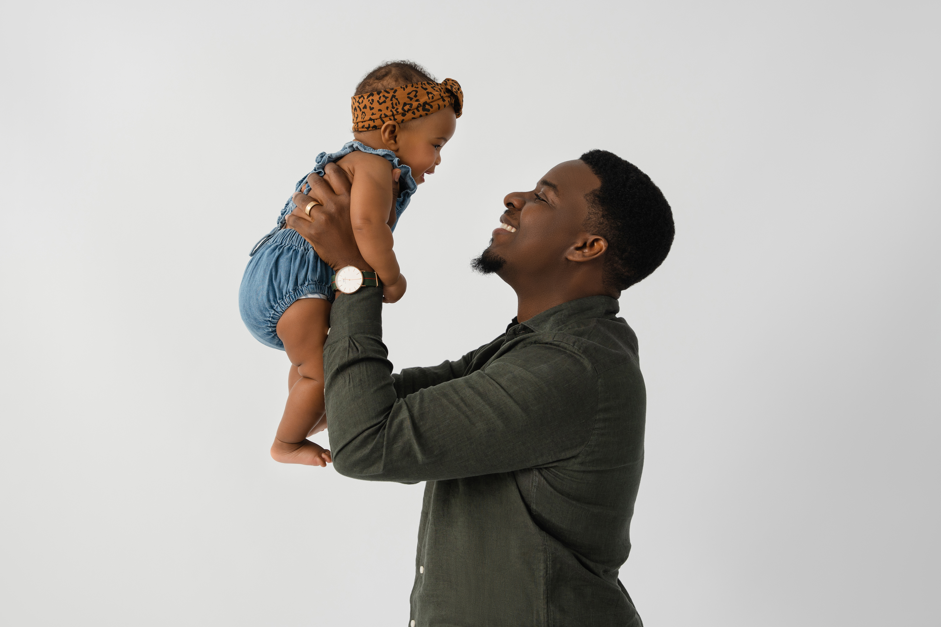 Warm studio portrait of a smiling father lifting his baby against a light gray background