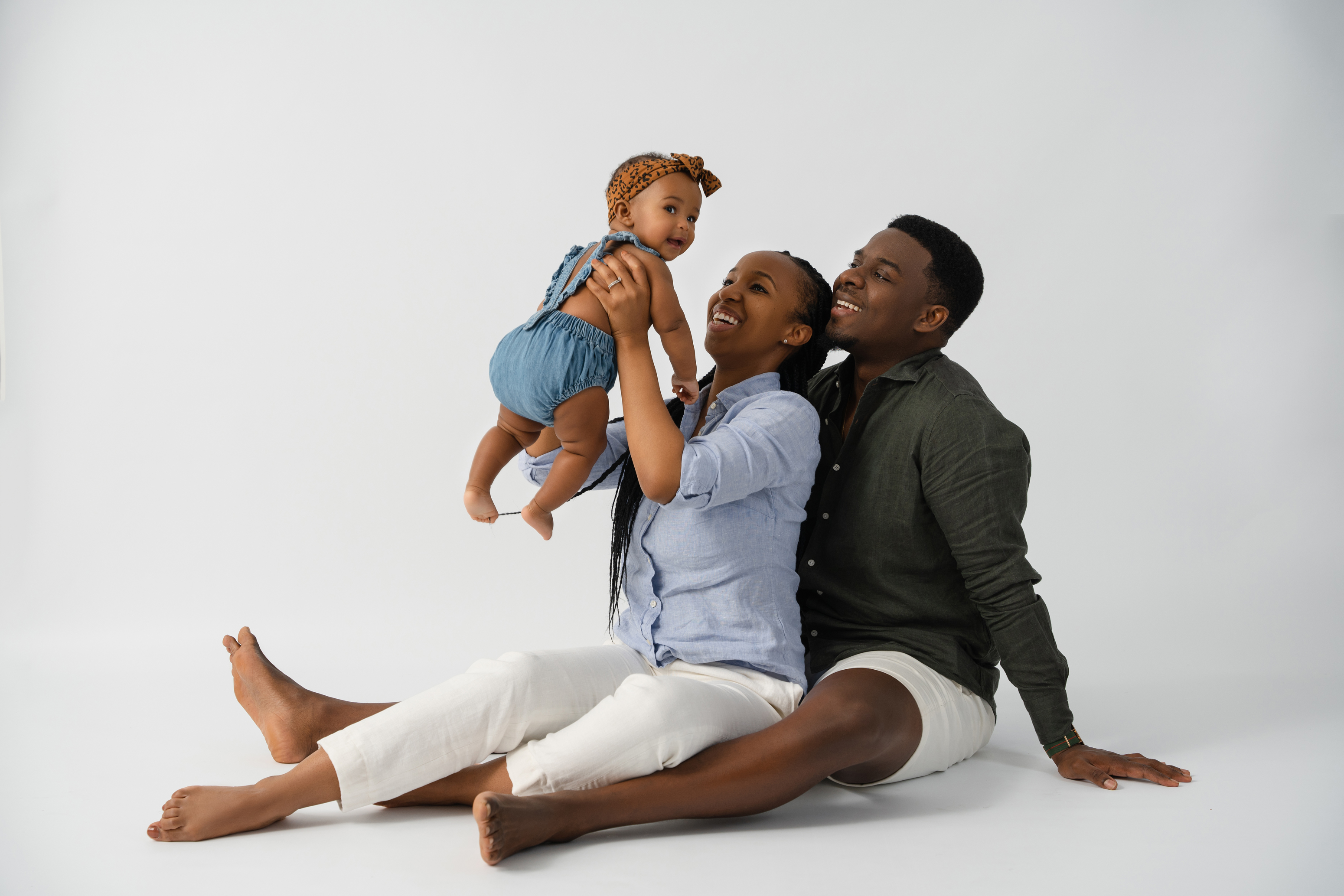 Relaxed studio family portrait of two parents seated with their baby against a neutral gray background