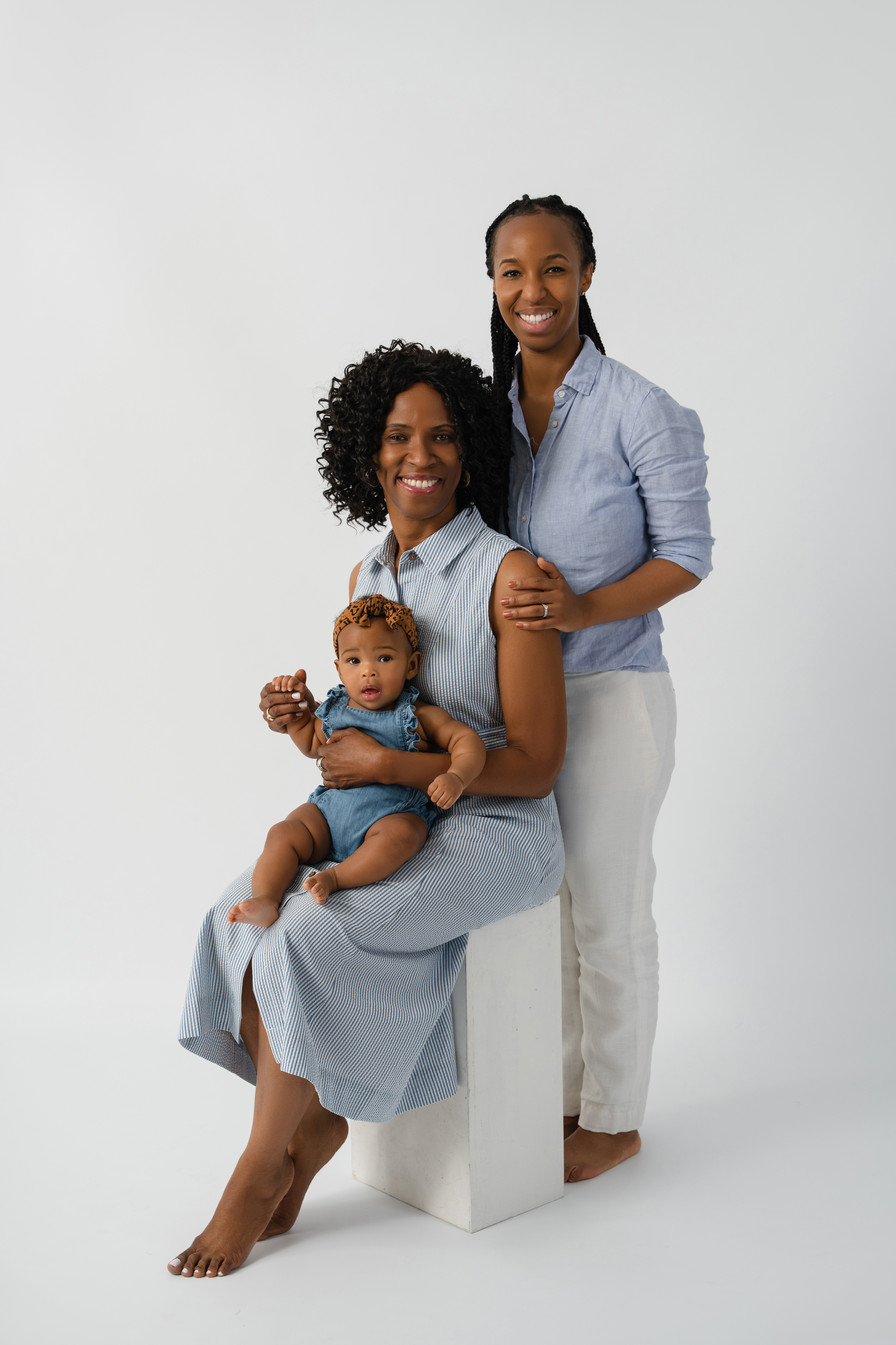 Multigenerational studio portrait of two women with a baby in coordinated blue and neutral clothing