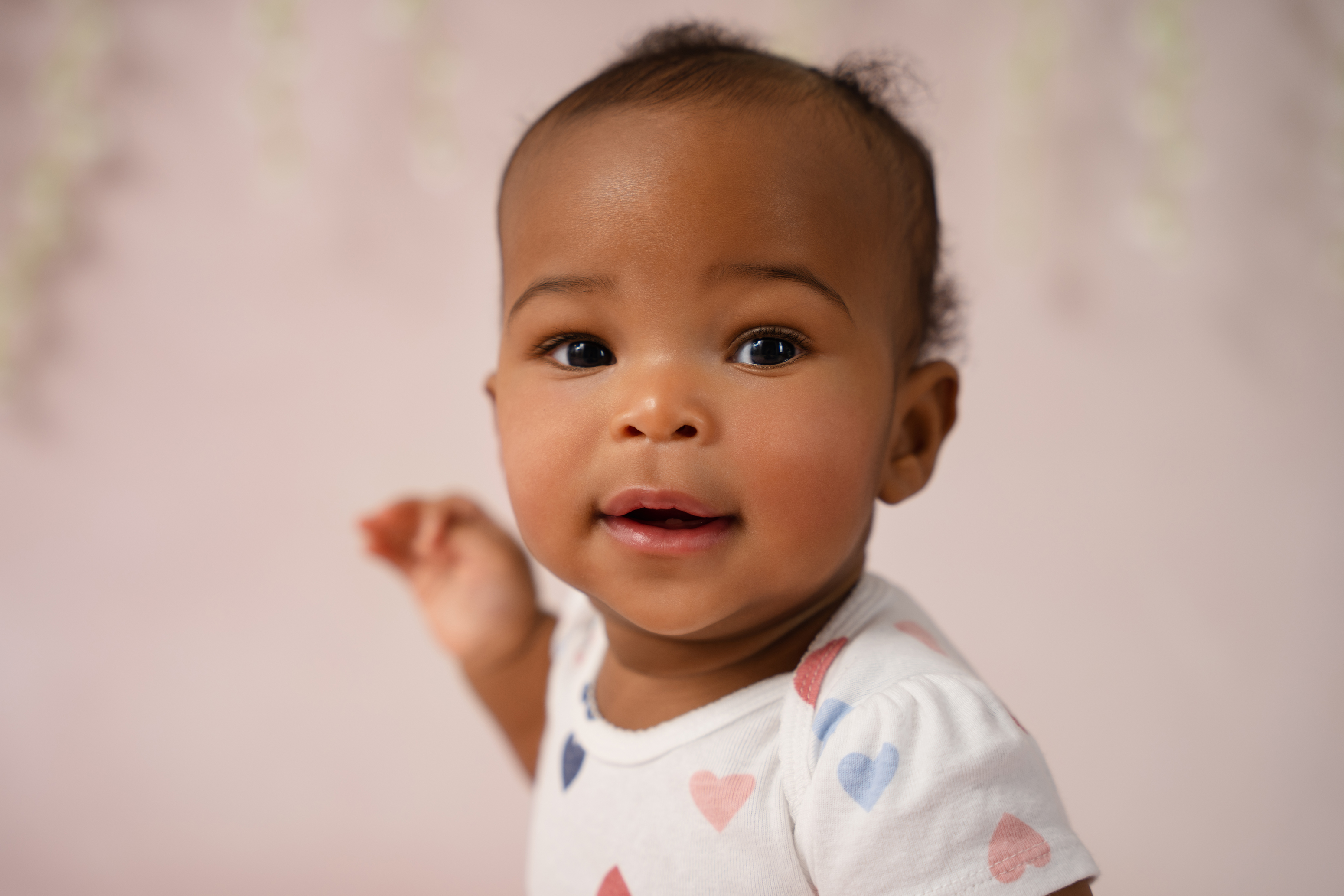 Close-up baby portrait against a soft pink background with delicate floral details 