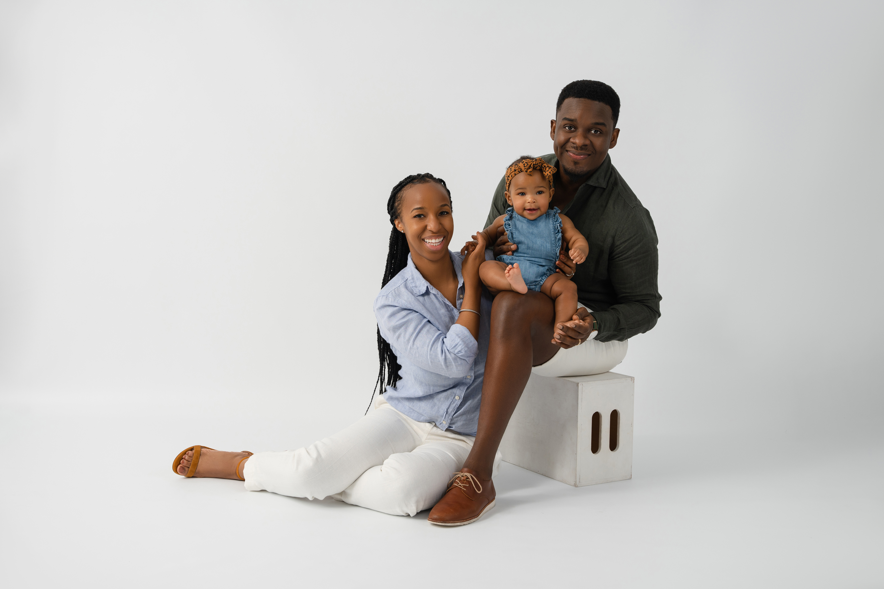 Studio family portrait of two parents with their baby seated together against a clean light gray background
