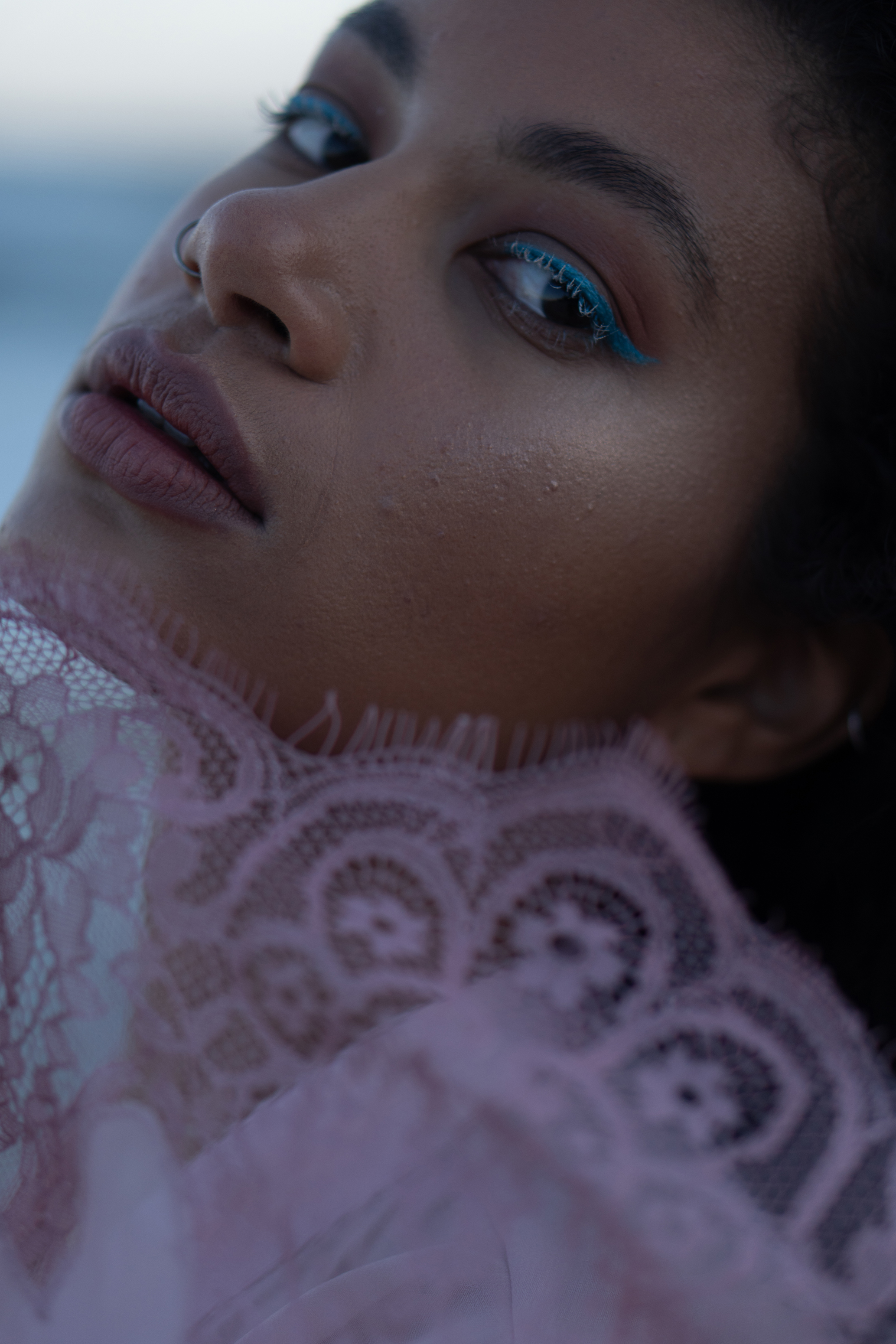 Raw close-up portrait of a woman framed by pink lace in cool natural light