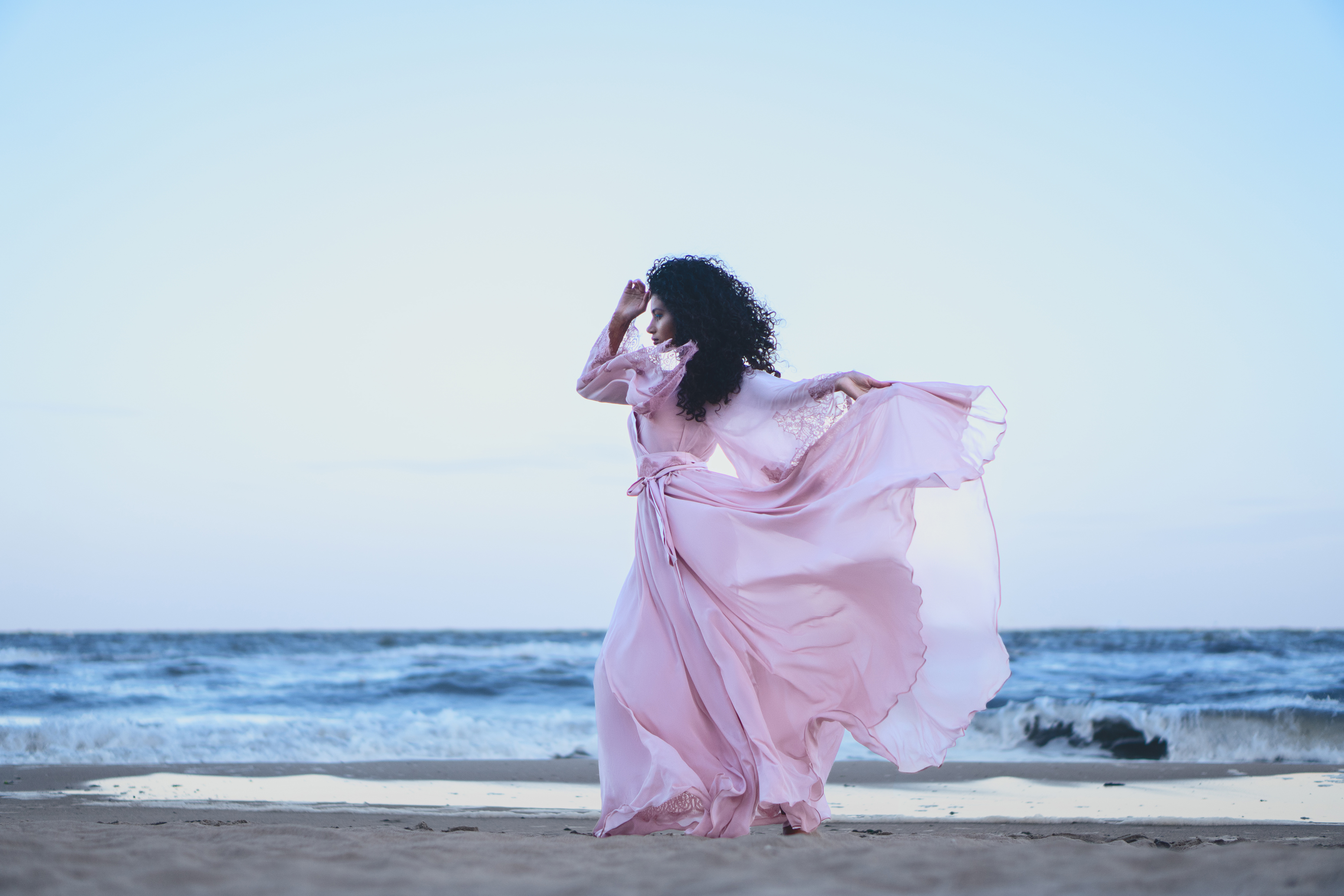 Final wide coastal fashion portrait with brighter skin, blush-pink fabric and cool blue seaside color grading