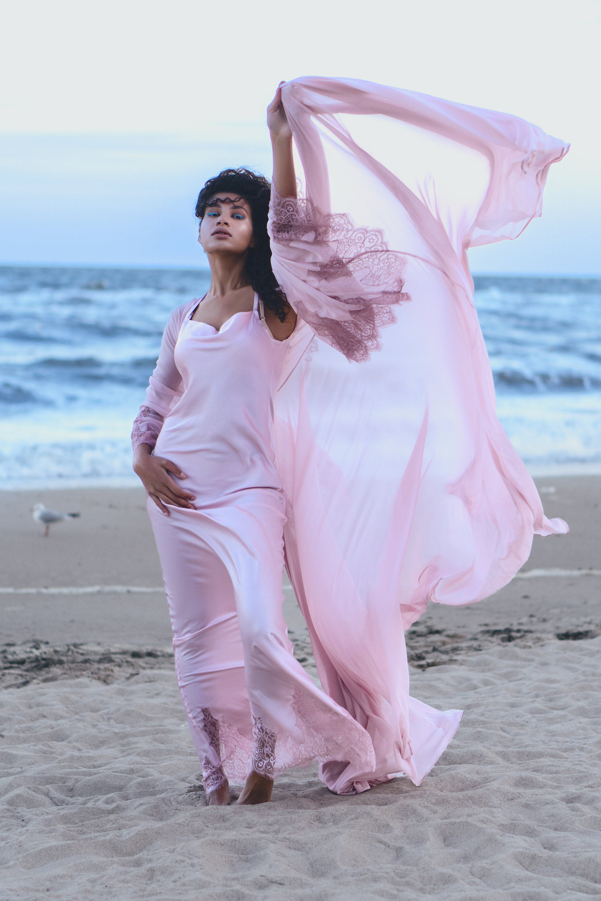 Final coastal fashion portrait with luminous skin, blush-pink fabric and soft blue seaside tones
