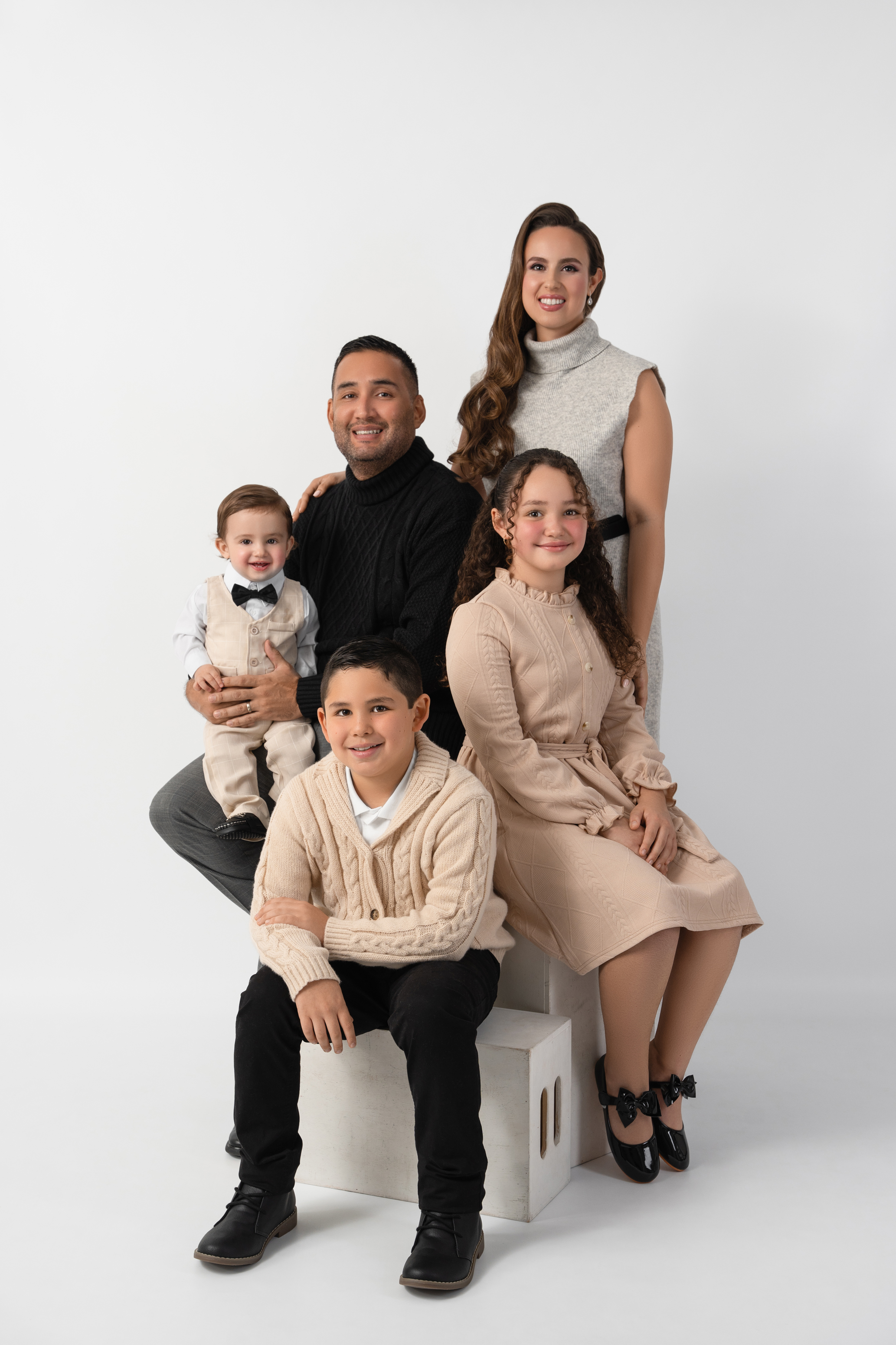 Light studio family portrait of two parents with three children in coordinated cream and neutral outfits