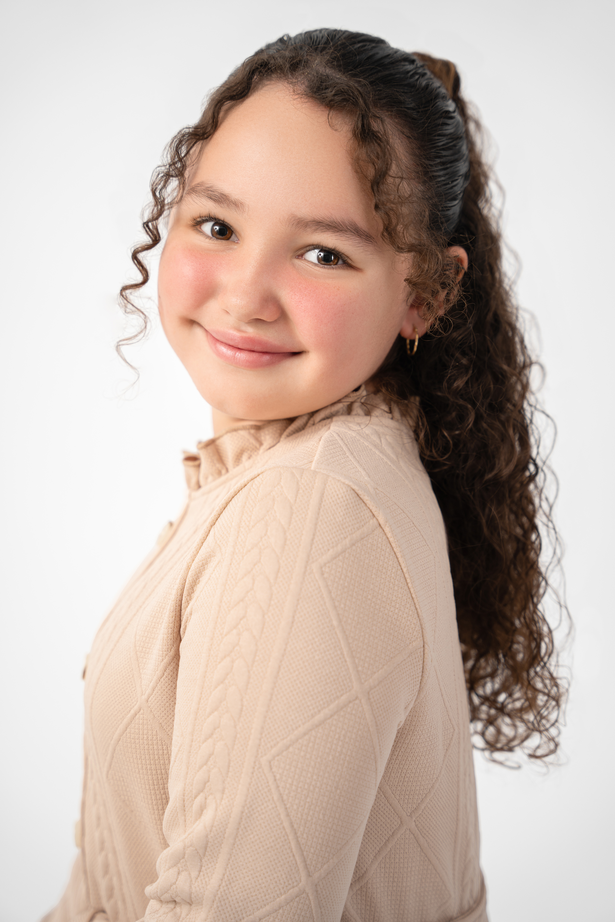 Soft studio portrait of a smiling girl in a cream knit top against a light neutral background