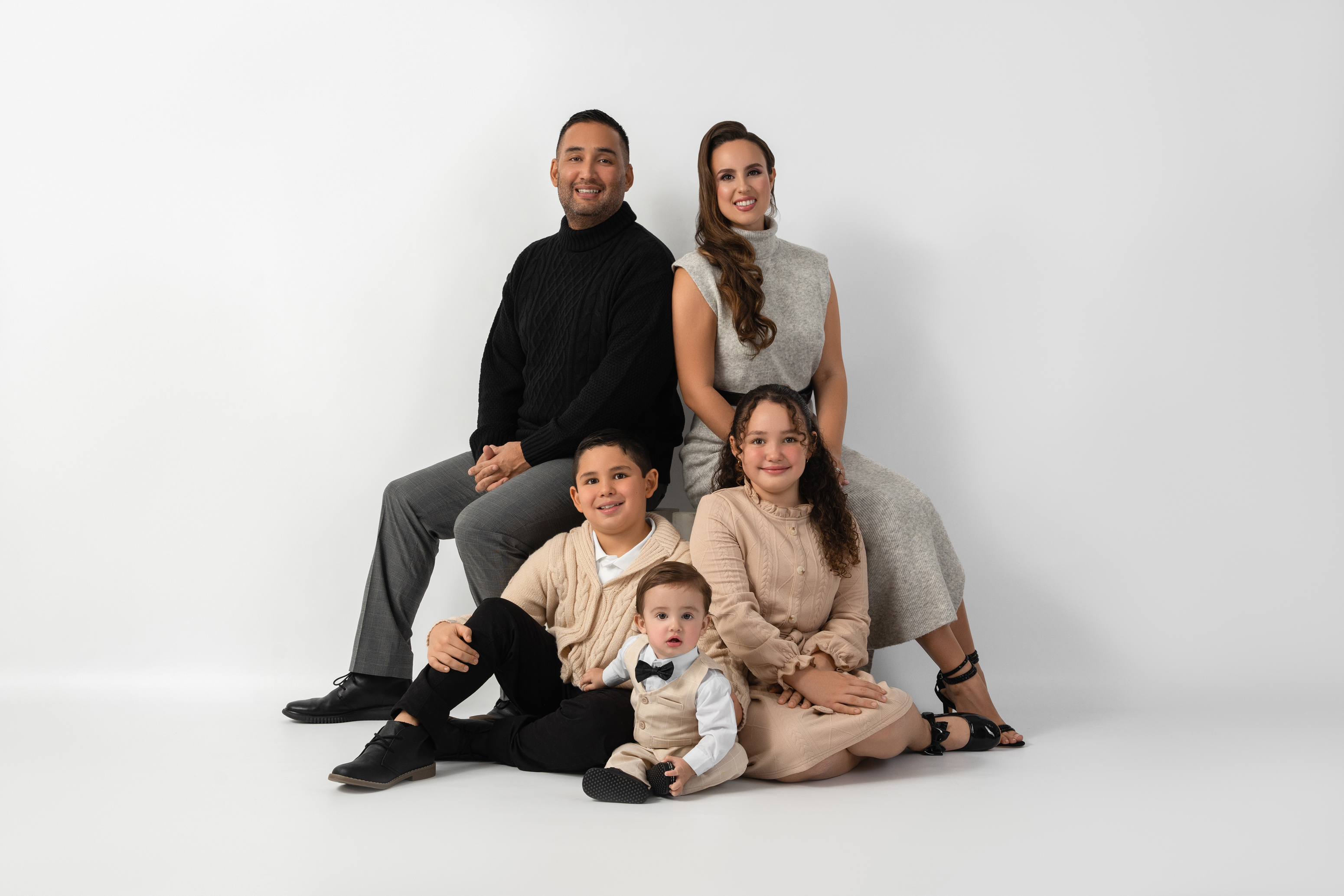 Relaxed family portrait of two parents and three children seated together in a bright studio