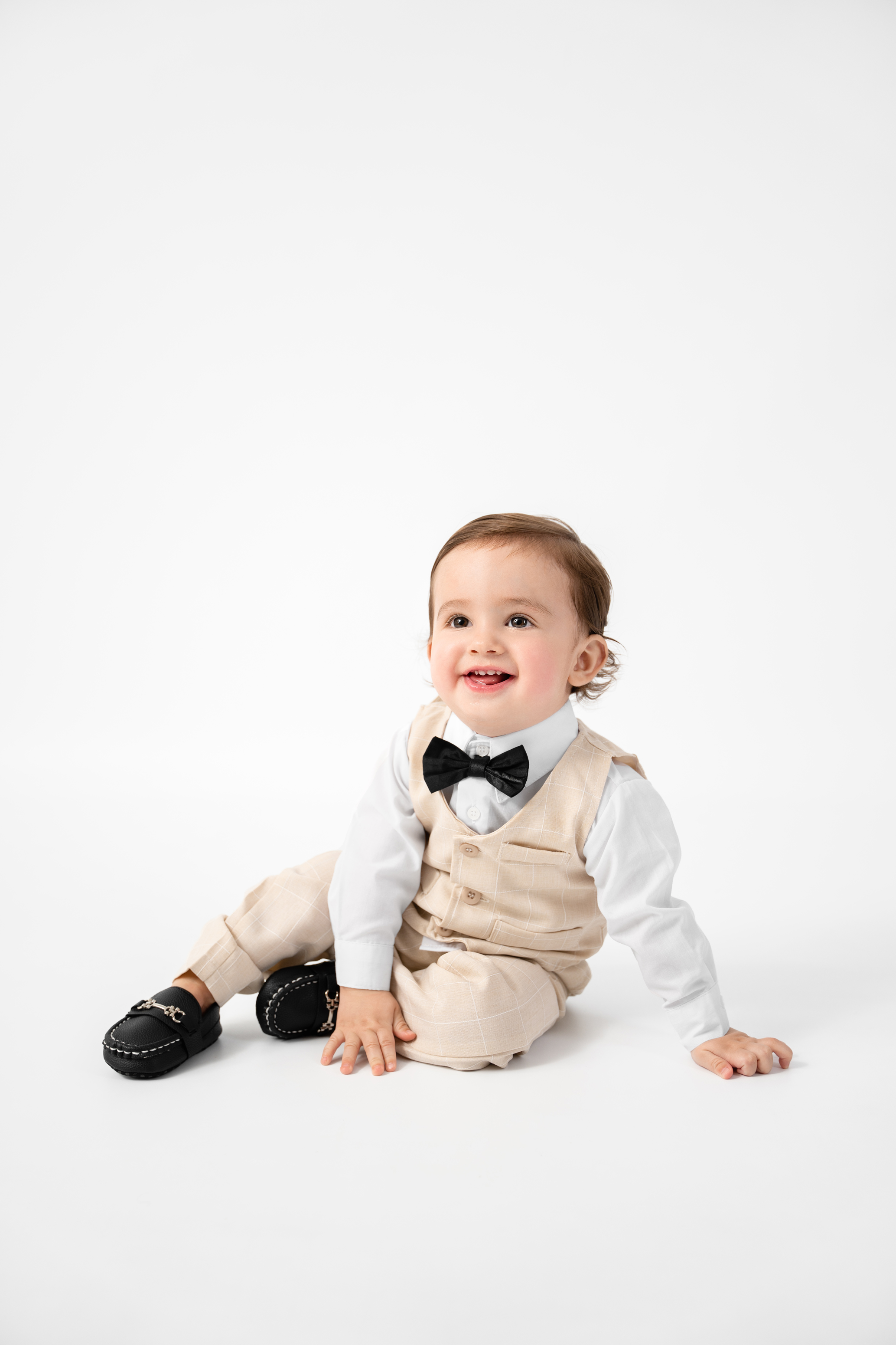 Studio baby portrait in a cream outfit with a black bow tie against a bright white background
