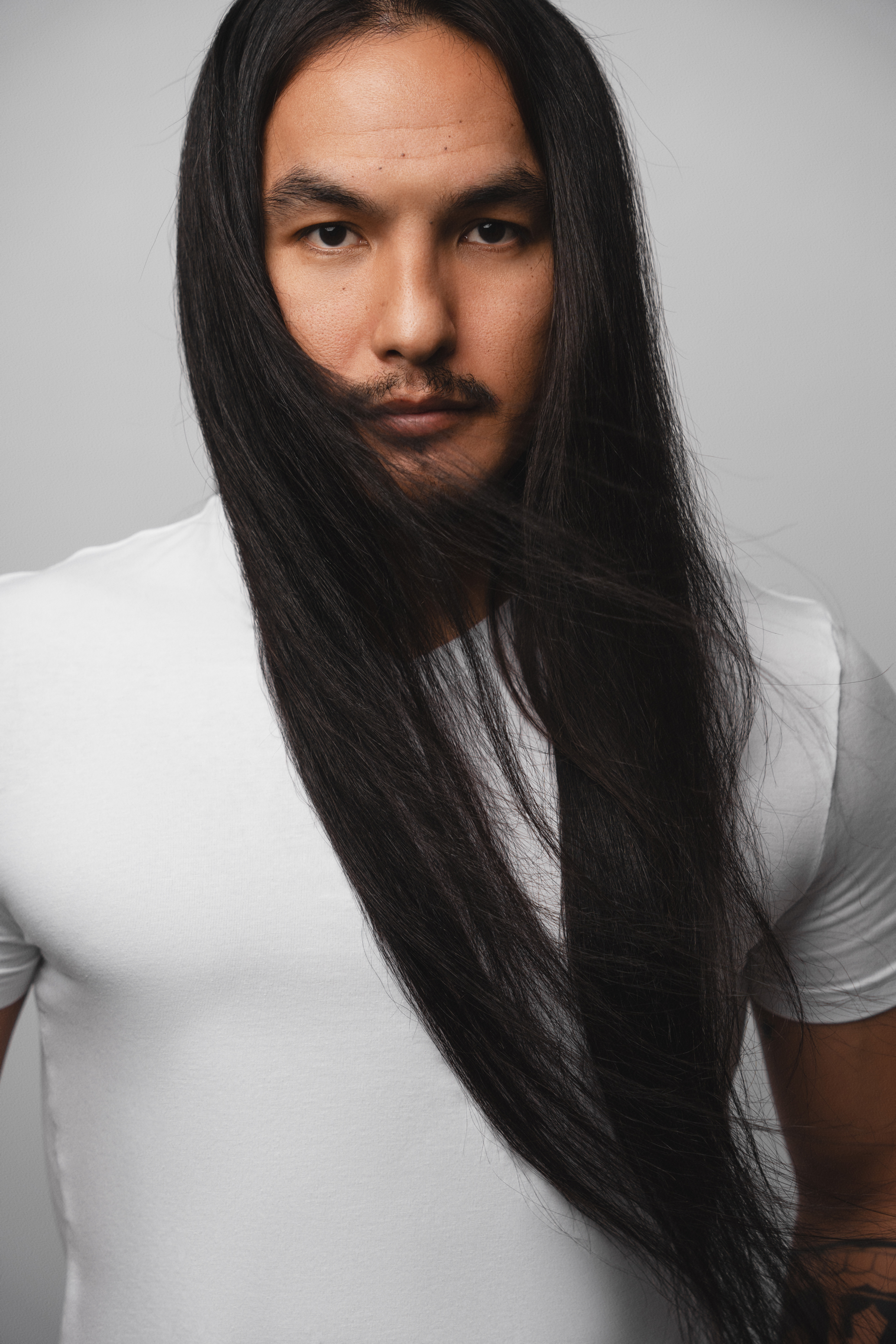 Close-up studio portrait of a long-haired man in a white T-shirt against a soft gray background