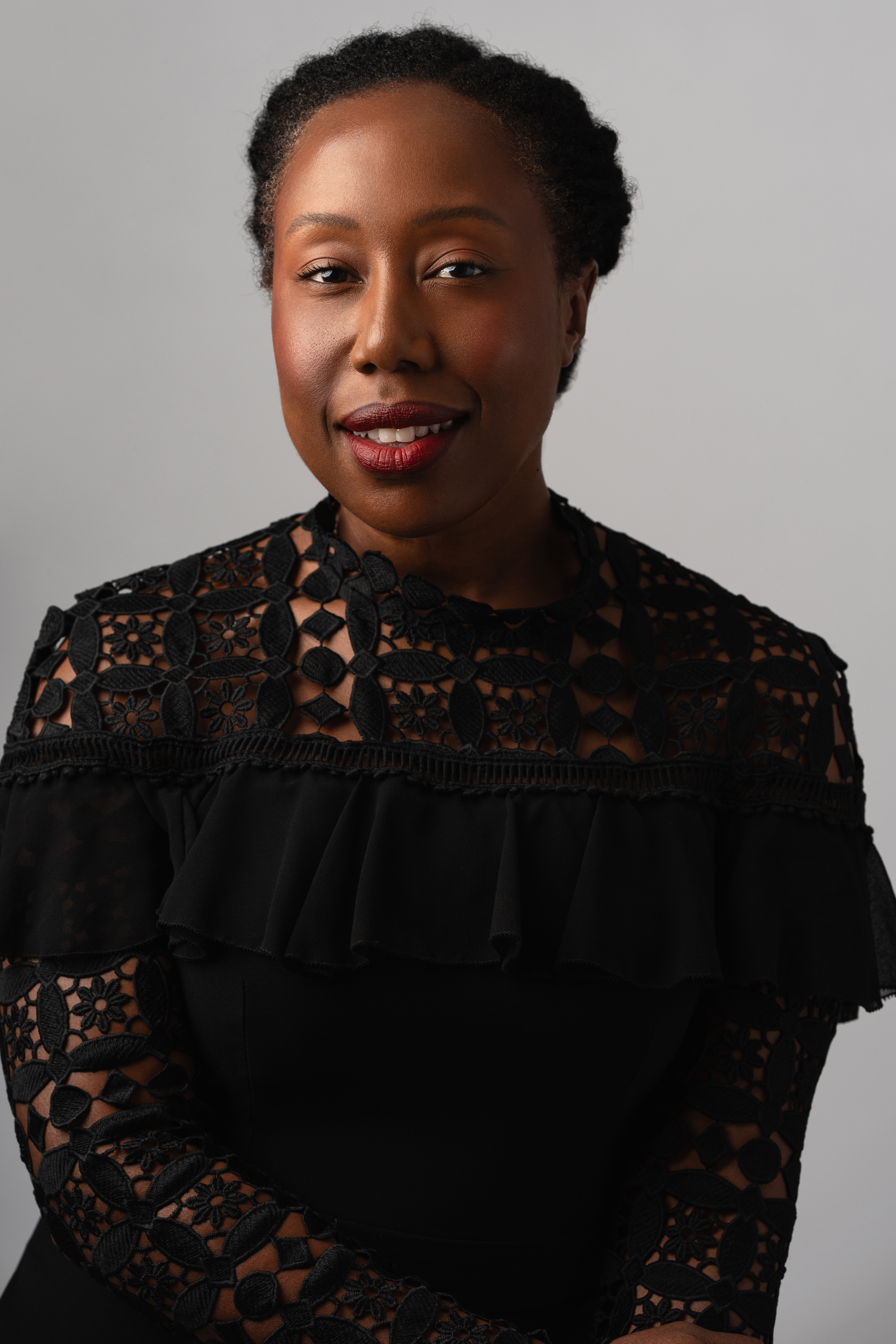 Close-up studio portrait of a woman in a black lace top against a soft gray background