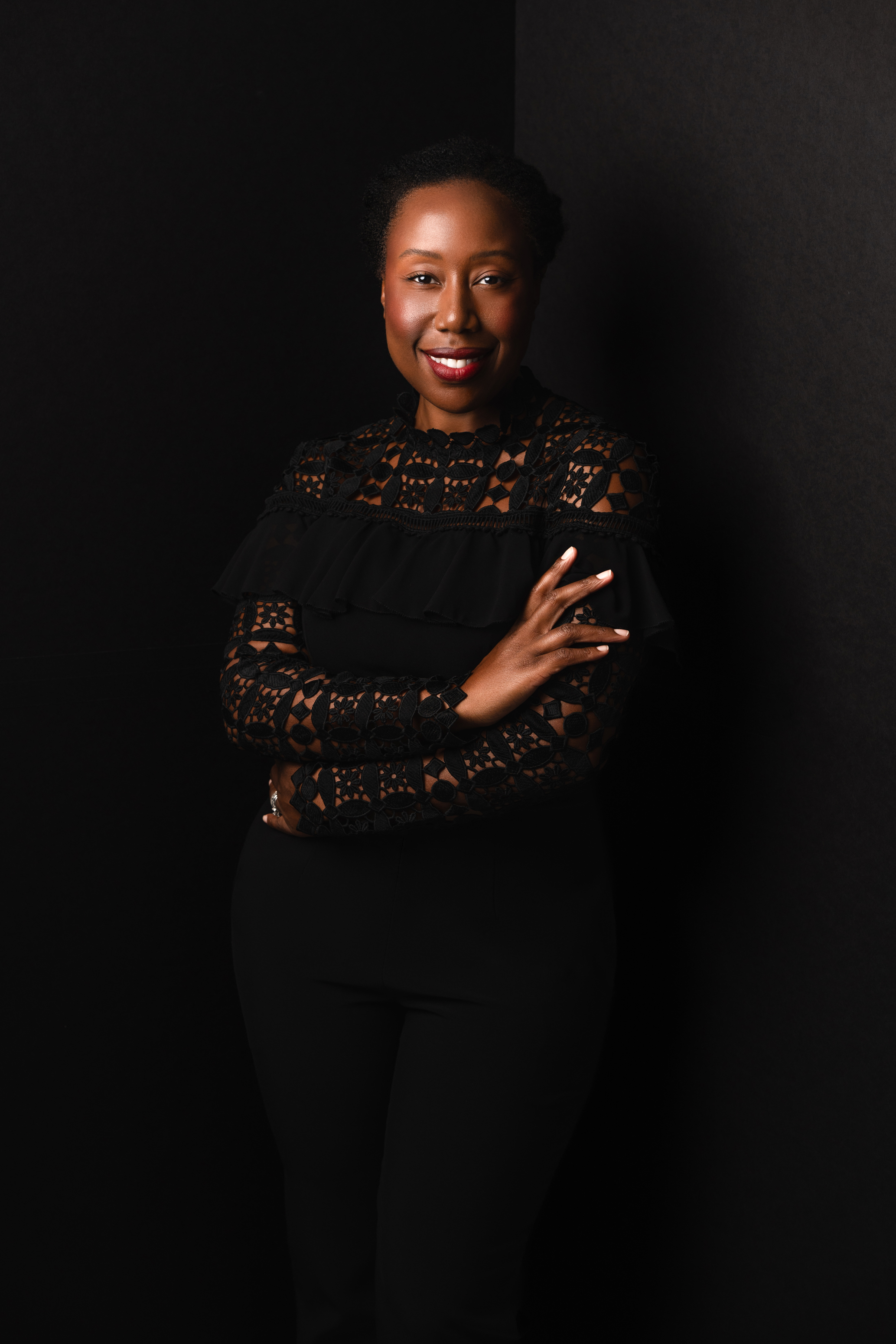 Full-length low-key studio portrait of a woman in a black lace outfit against a dark background