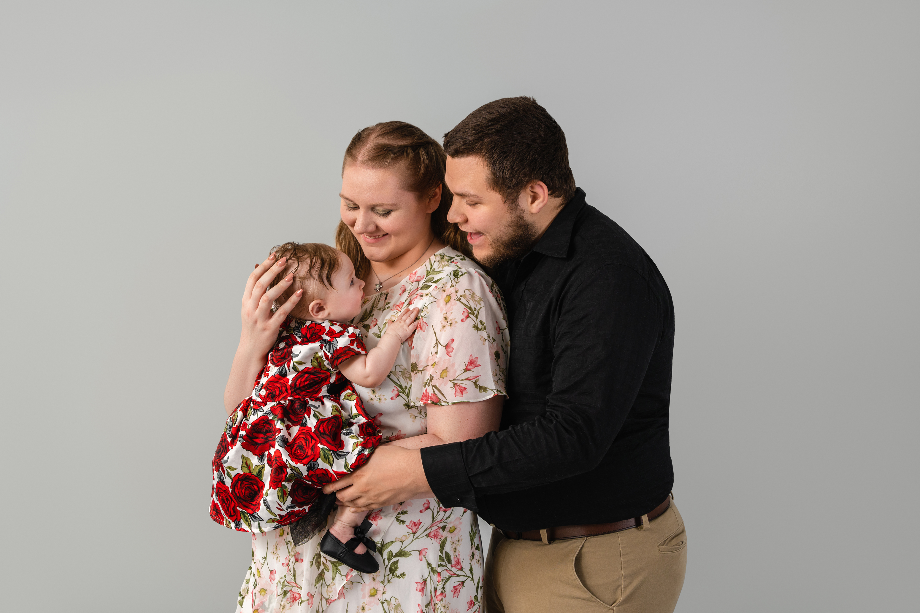 Candid studio family portrait of two parents embracing their young child against a neutral gray background