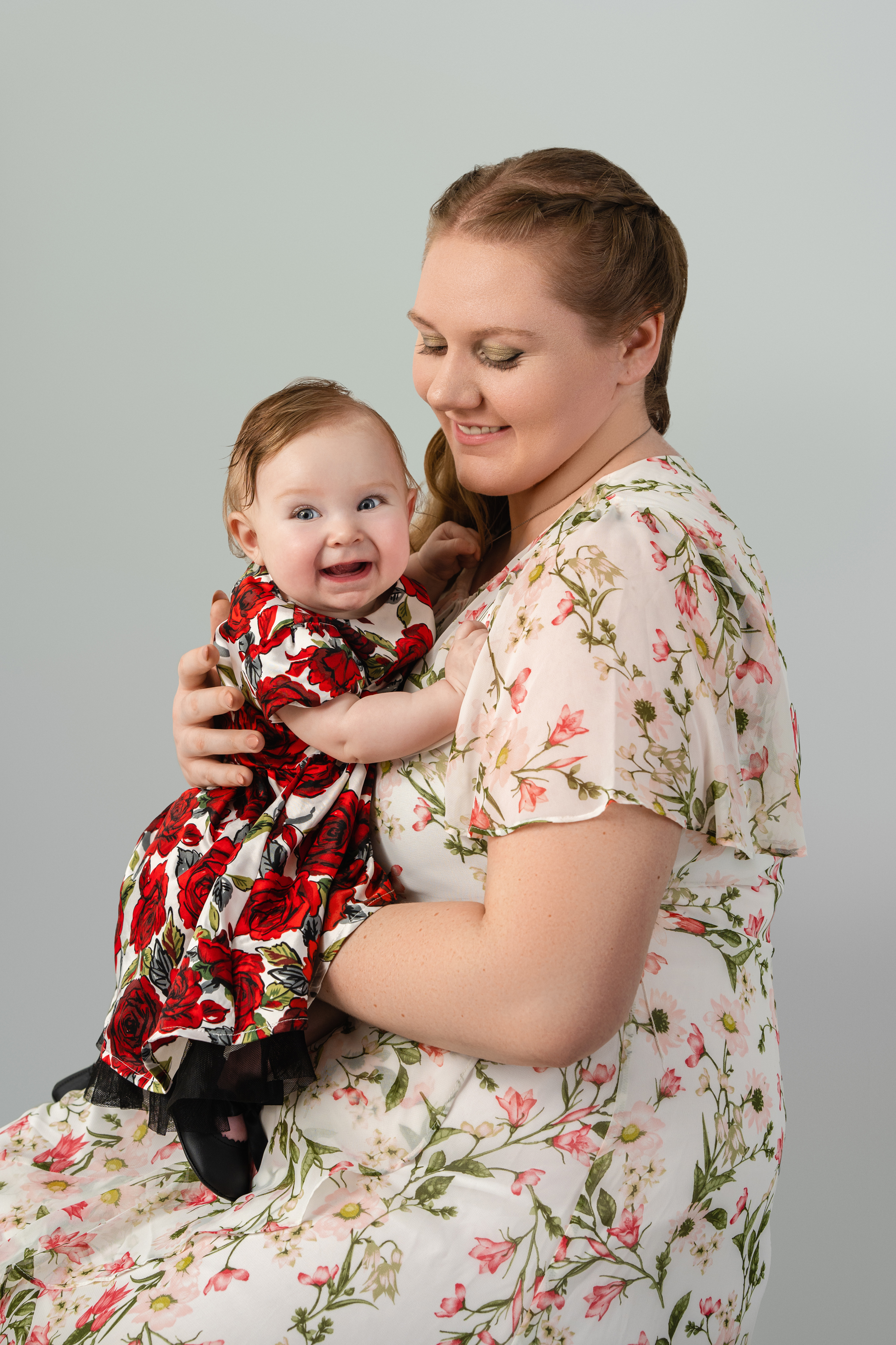 Studio portrait of a mother holding her smiling baby in a red floral dress