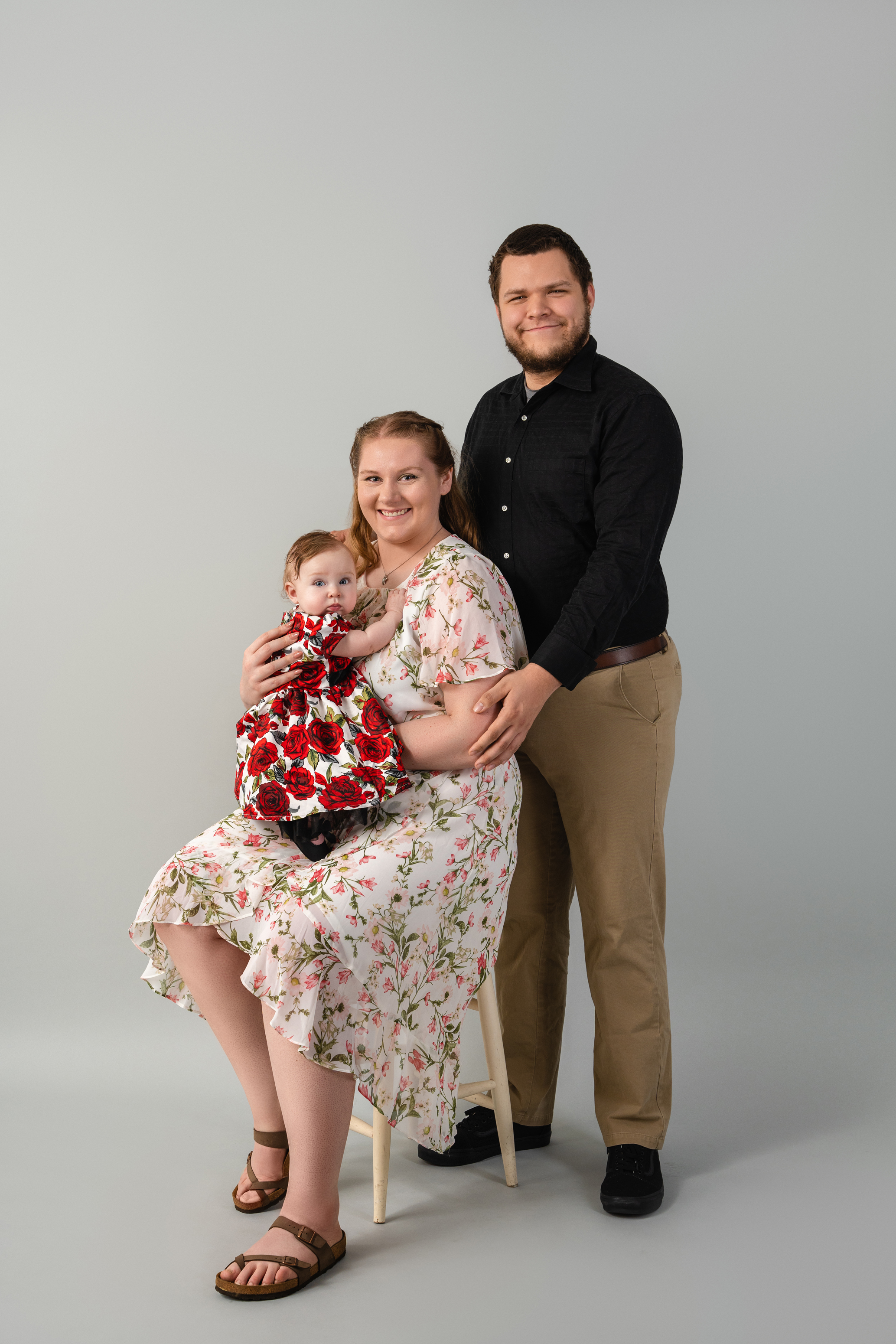 Full-length studio family portrait of two parents with their baby against a neutral gray background