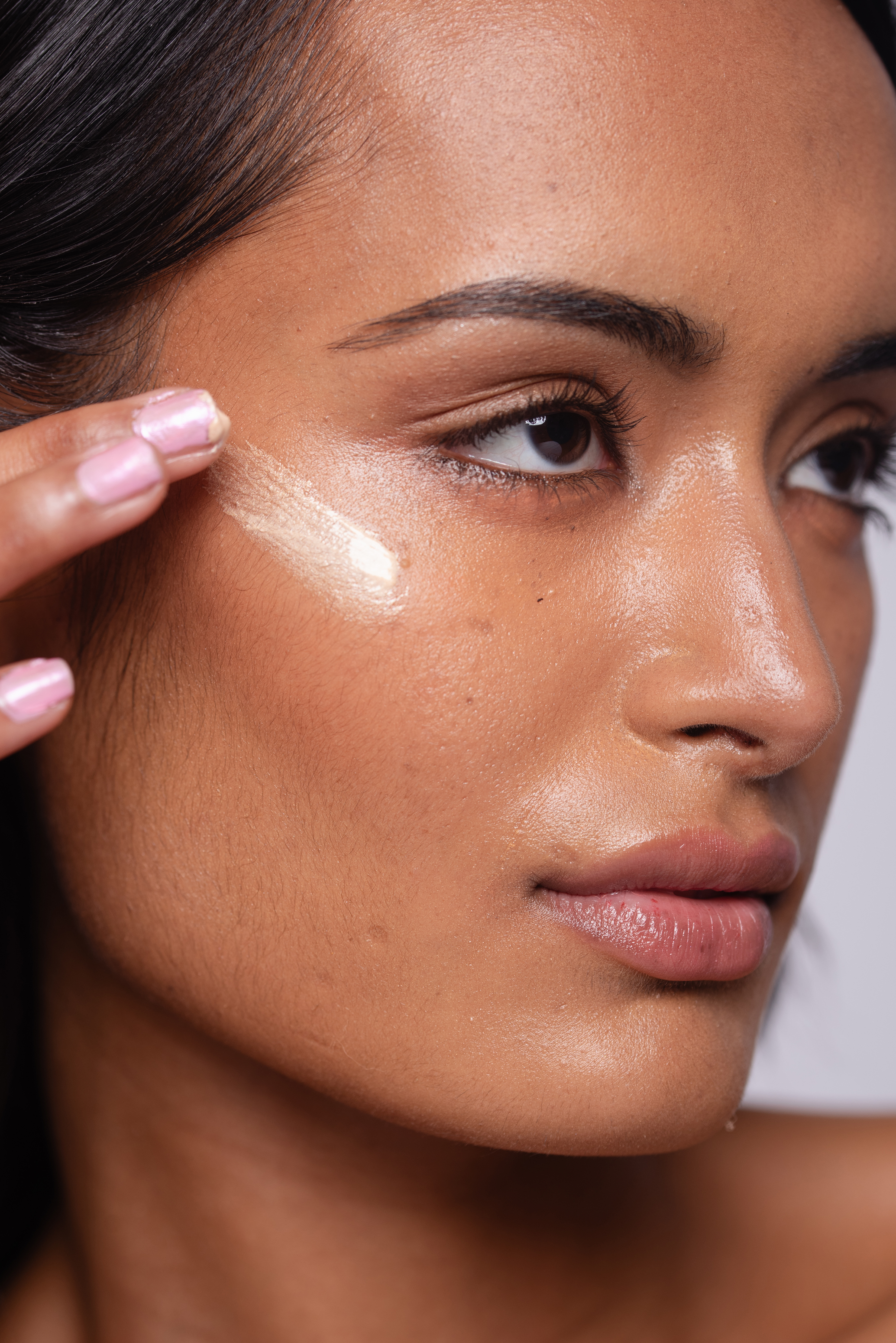 Beauty close-up before final retouching, showing natural skin texture, glossy makeup and a hand applying product beneath the eye