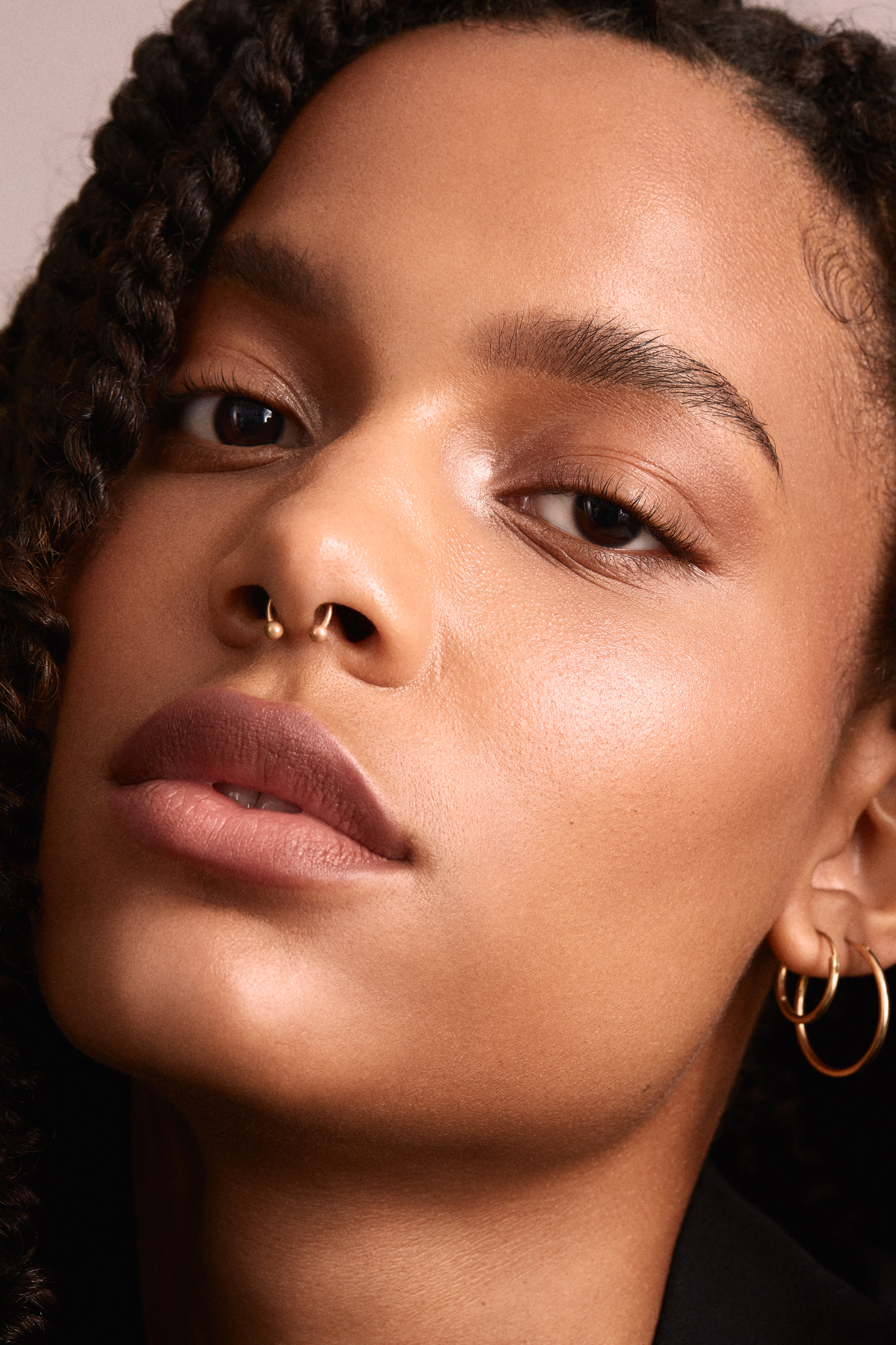 Close-up beauty portrait with warm luminous skin, neutral makeup and soft dusty-pink tones