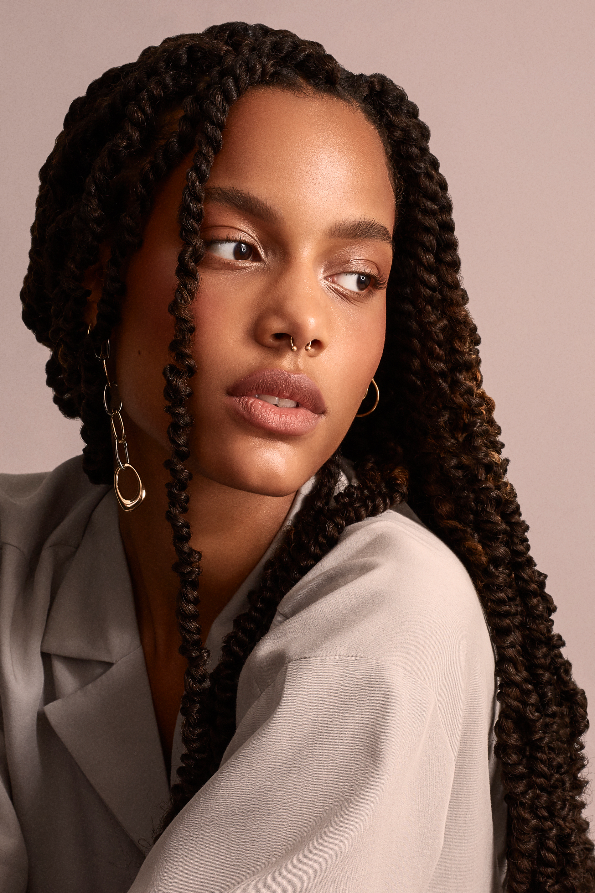 Beauty portrait with long braids, warm skin tones and a muted dusty-pink background