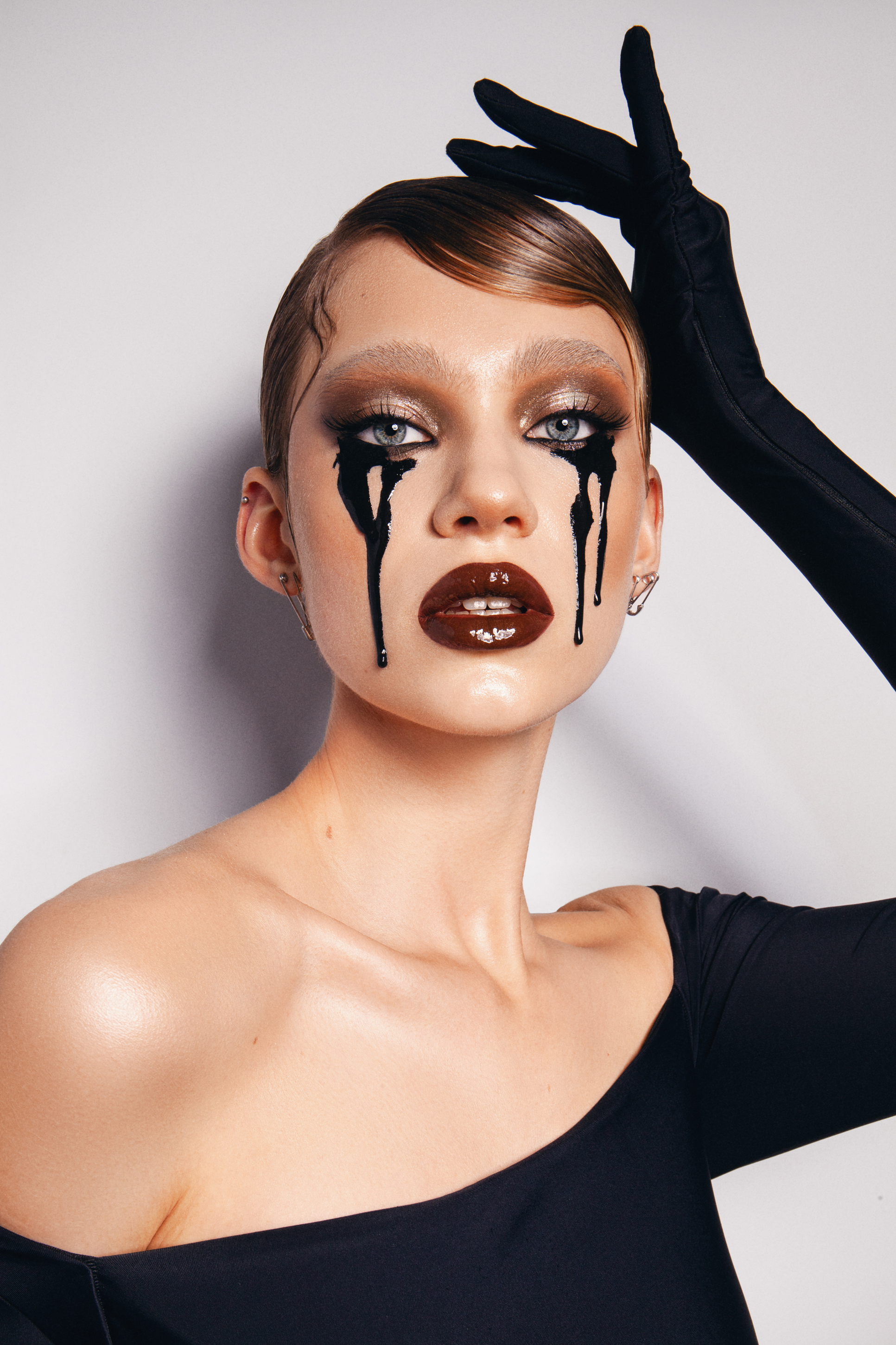 Editorial beauty portrait with dramatic black eye makeup, glossy dark lips and graphic black details beneath the eyes