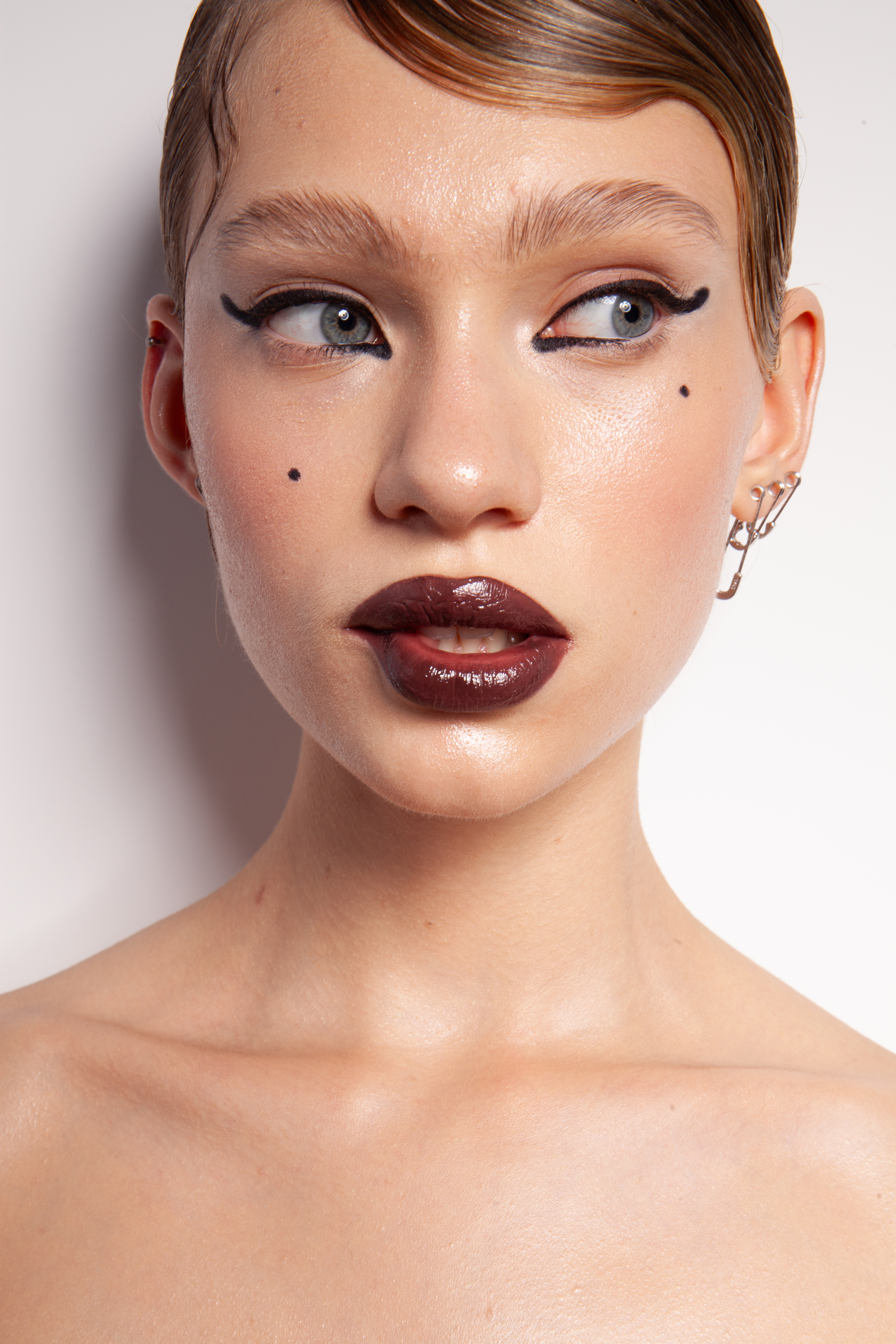 Beauty close-up before retouching, with sharp black eyeliner, glossy burgundy lips and sculpted brows