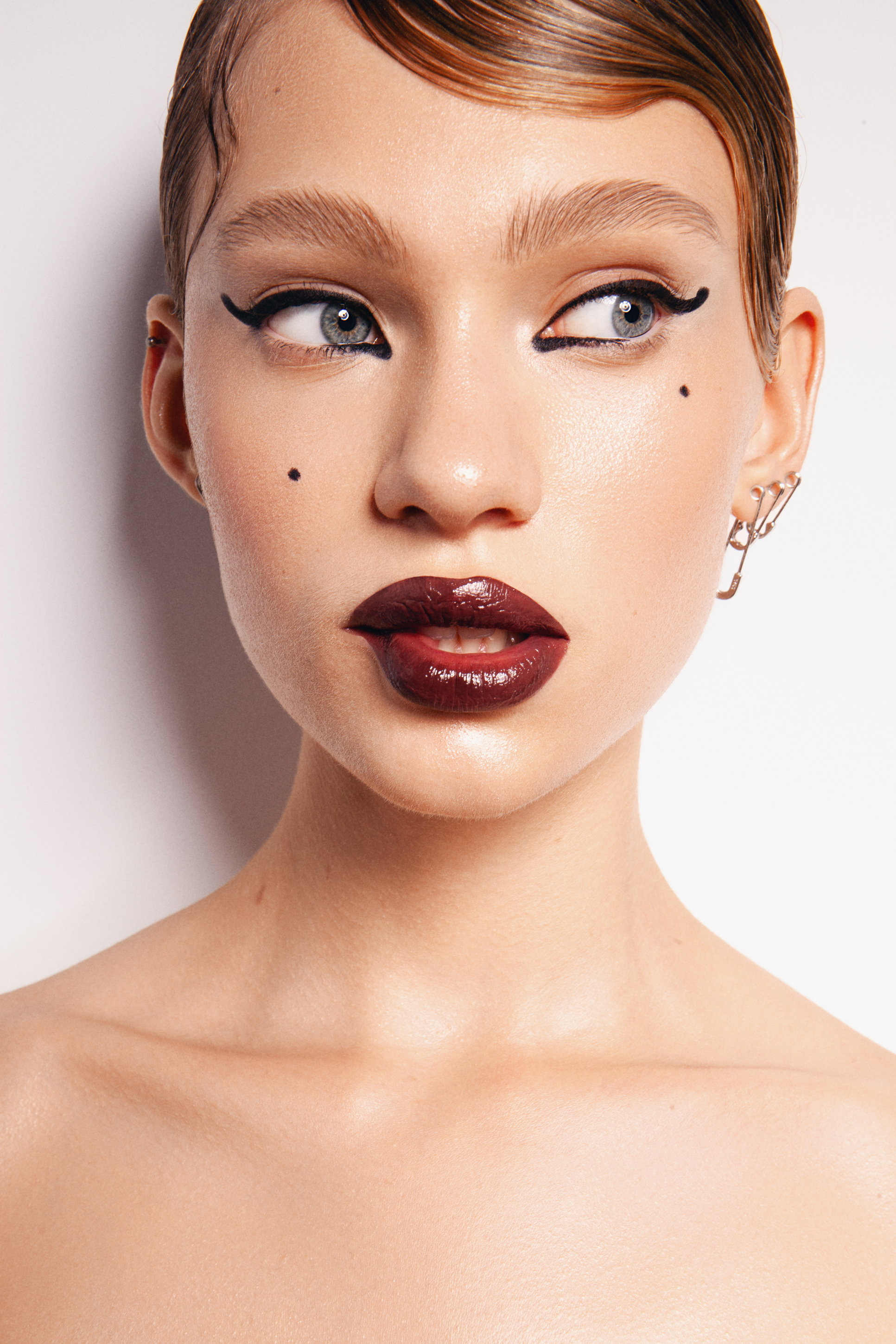 Beauty close-up with sharp graphic eyeliner, glossy burgundy lips and clean luminous skin