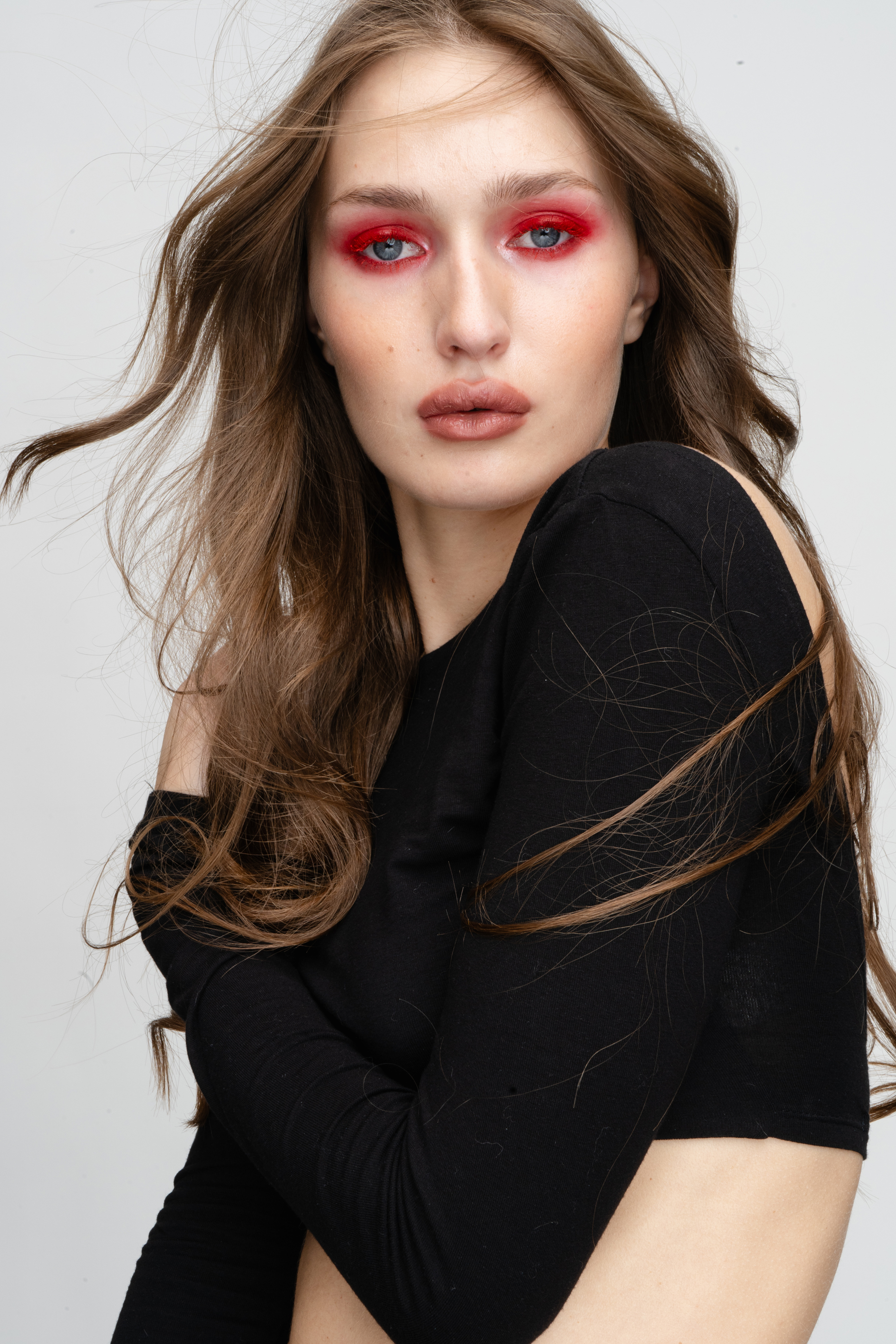 Beauty portrait before retouching, with vivid crimson eye makeup, loose brown hair and a black long-sleeve top