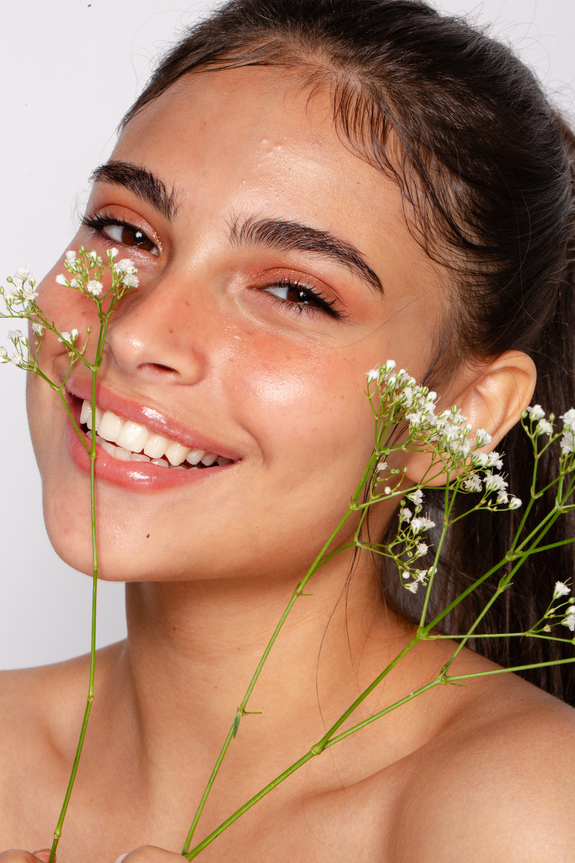 Beauty portrait before retouching, showing a smiling woman framed by delicate white flowers with warm natural skin tones
