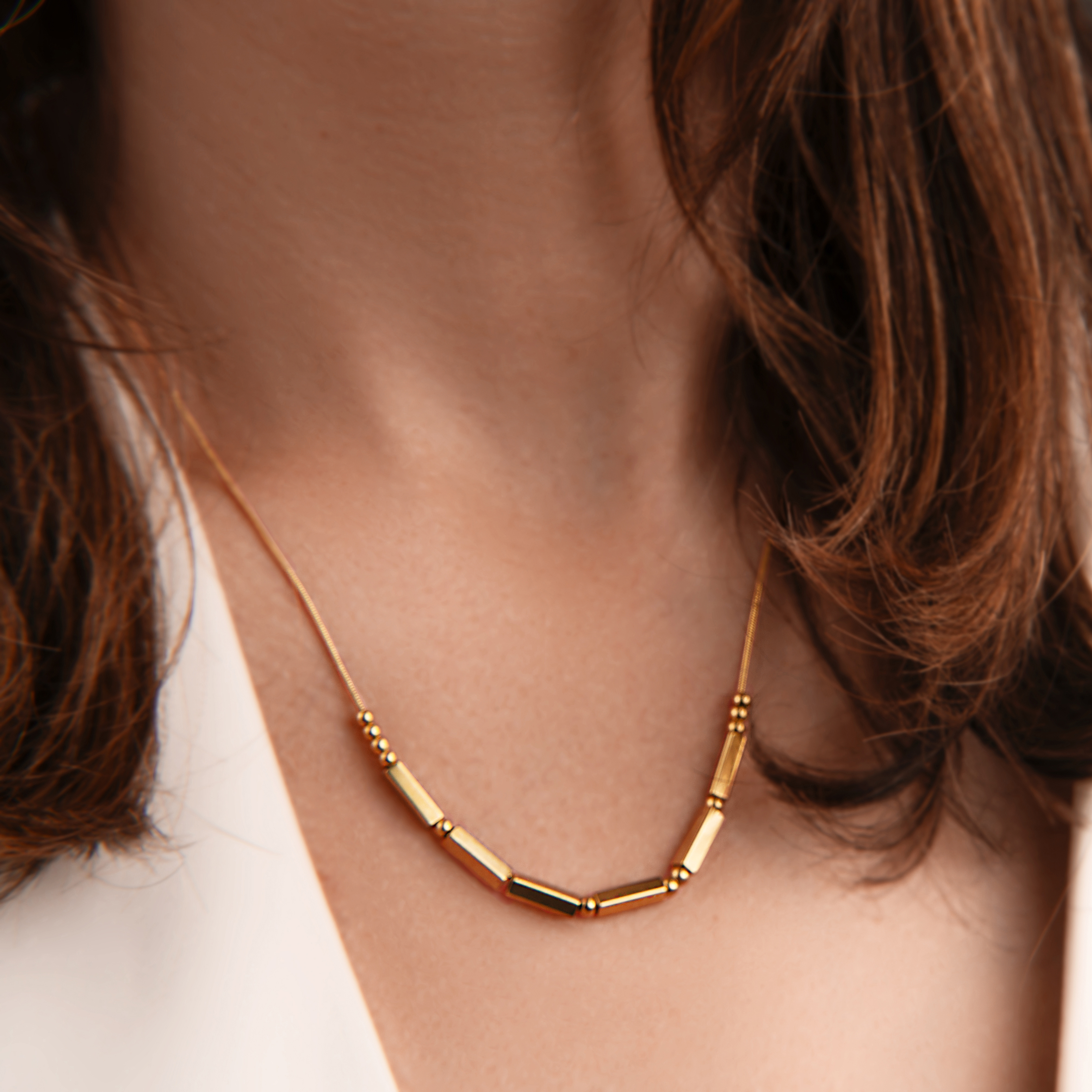 Close-up jewelry image of a minimal gold necklace with warm balanced skin tones and clean product detail